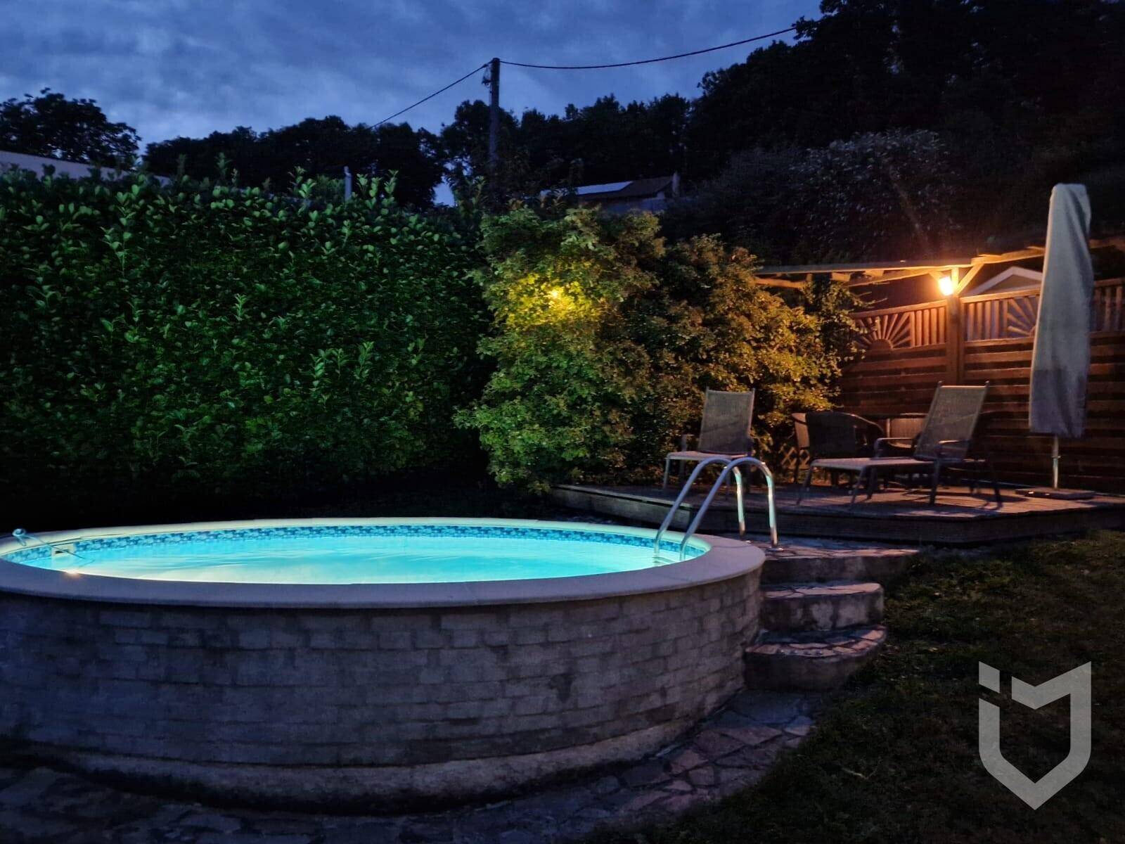 Beleuchteter Aufstellpool und gemütlicher Sitzbereich im Garten bei Nacht.