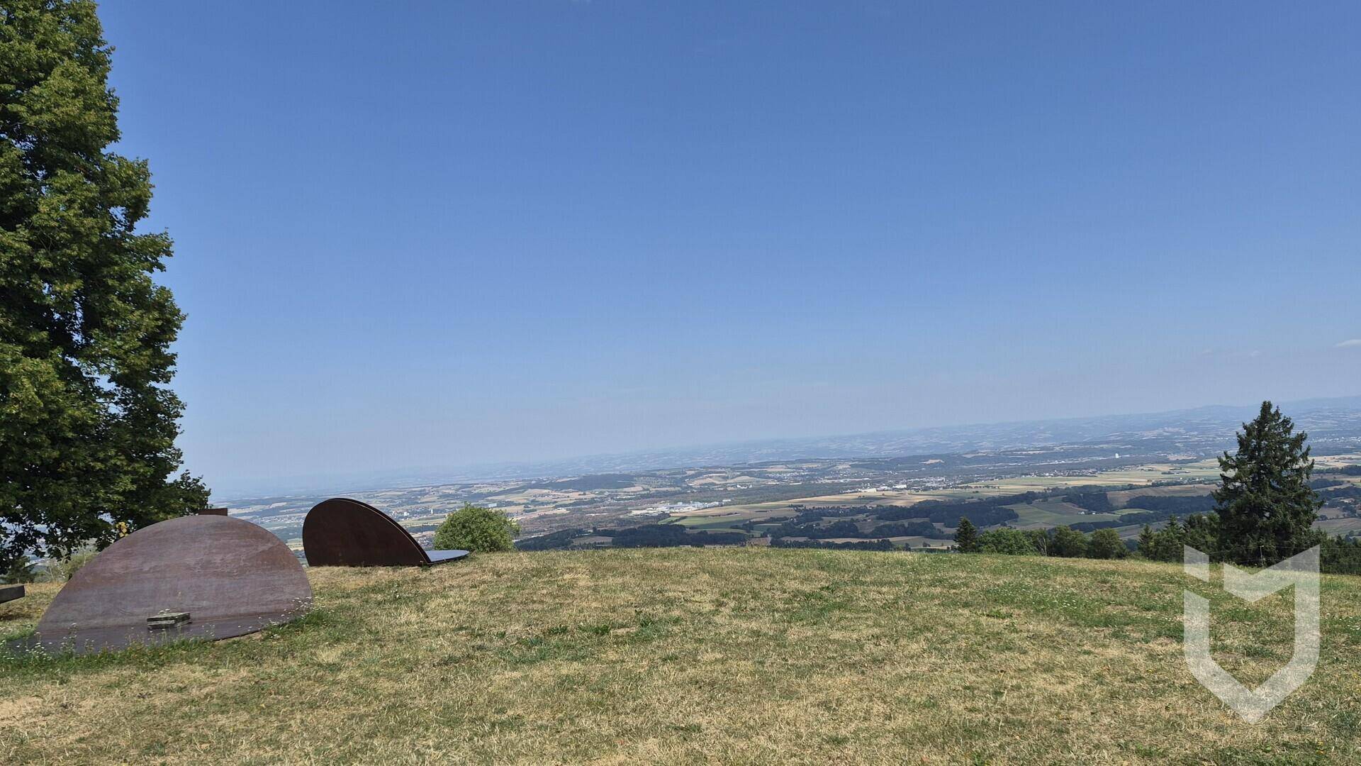 Panoramablick von einem Hügel über eine weite Landschaft mit Feldern und Siedlungen unter klarem Himmel.