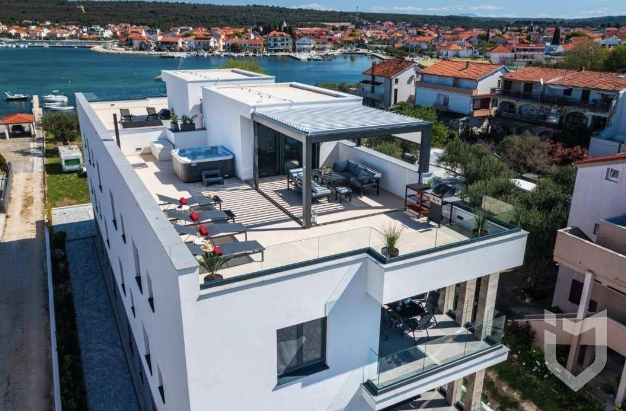 Luftaufnahme eines modernen Gebäudes mit großer Dachterrasse, Whirlpool und Meerblick.