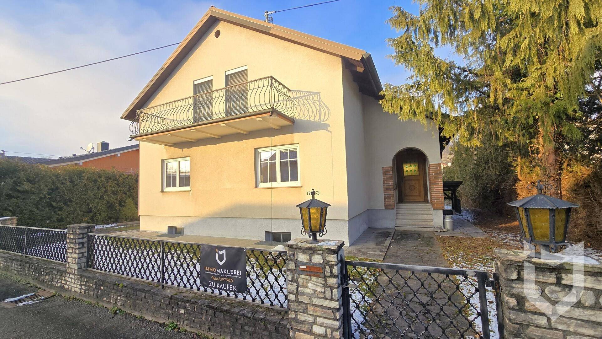 Vorderansicht des Einfamilienhauses mit Balkon und gepflegtem Vorgarten an einem sonnigen Tag.
