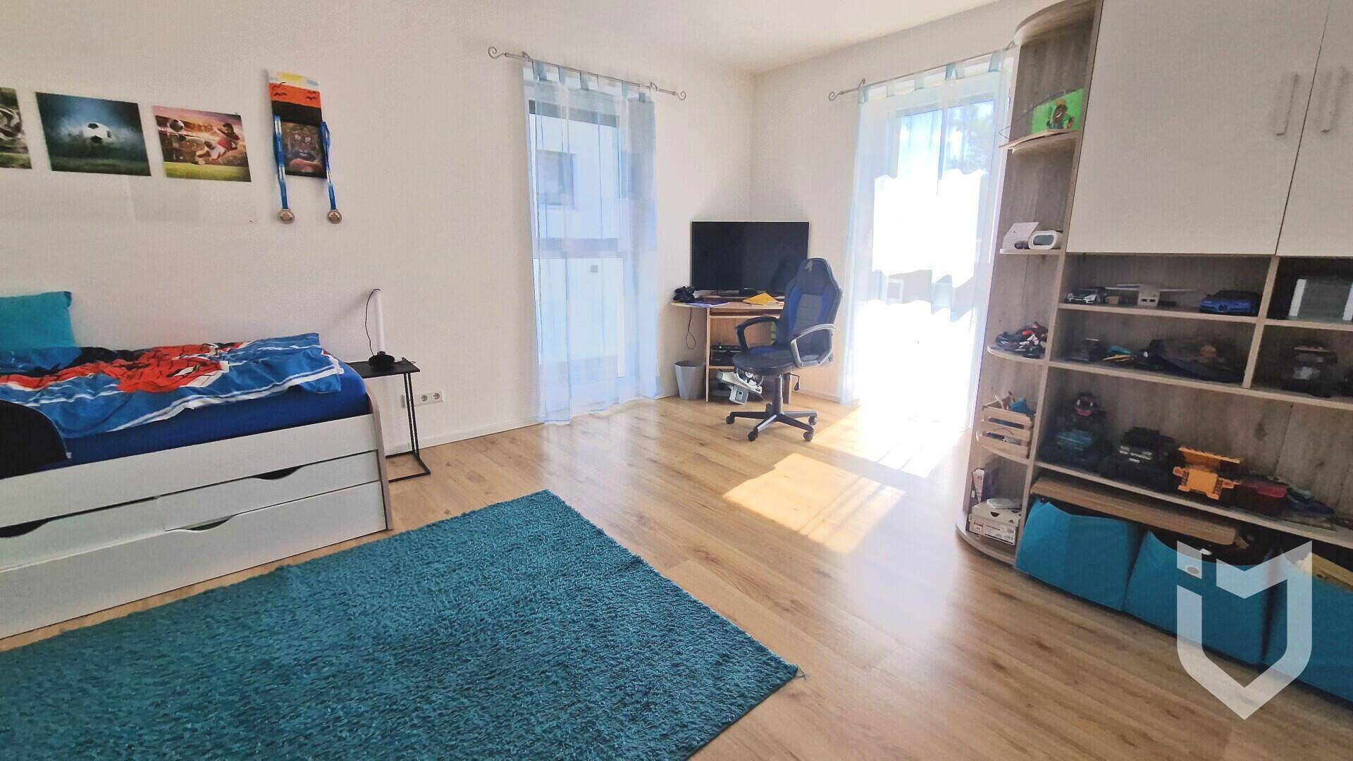 Helles Kinderzimmer mit Holzboden, Schreibtisch und Zugang zum Balkon oder Garten.