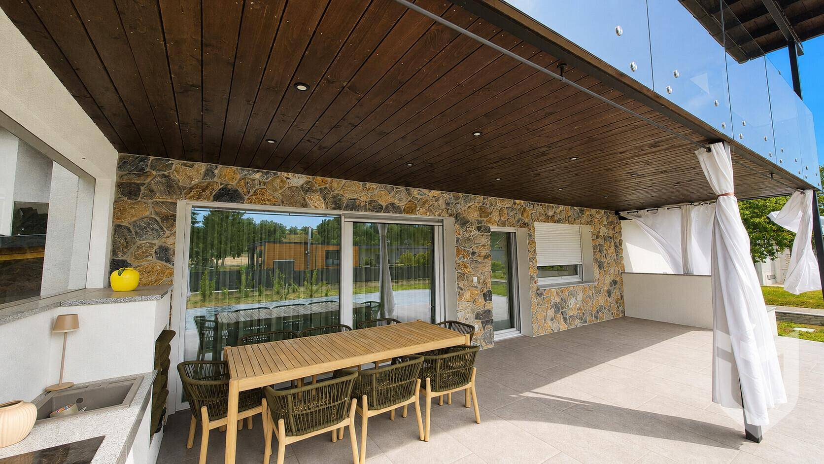 Überdachte Terrasse mit Steinfassade, Holzdach und Esstisch für Mahlzeiten im Freien.