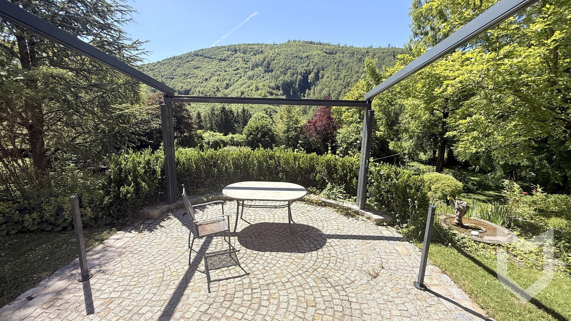 Gepflasterte Terrasse mit Sitzgelegenheiten unter einer Pergola und Blick auf die grüne Hügellandschaft.