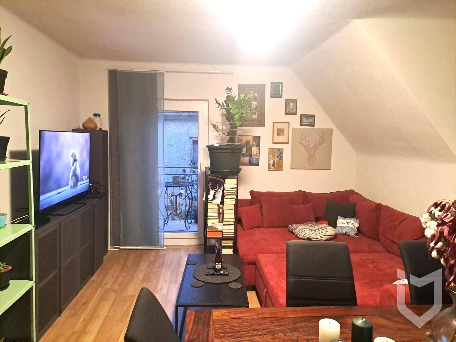Gemütliches Wohnzimmer im Dachgeschoss mit rotem Ecksofa und Balkonzugang.