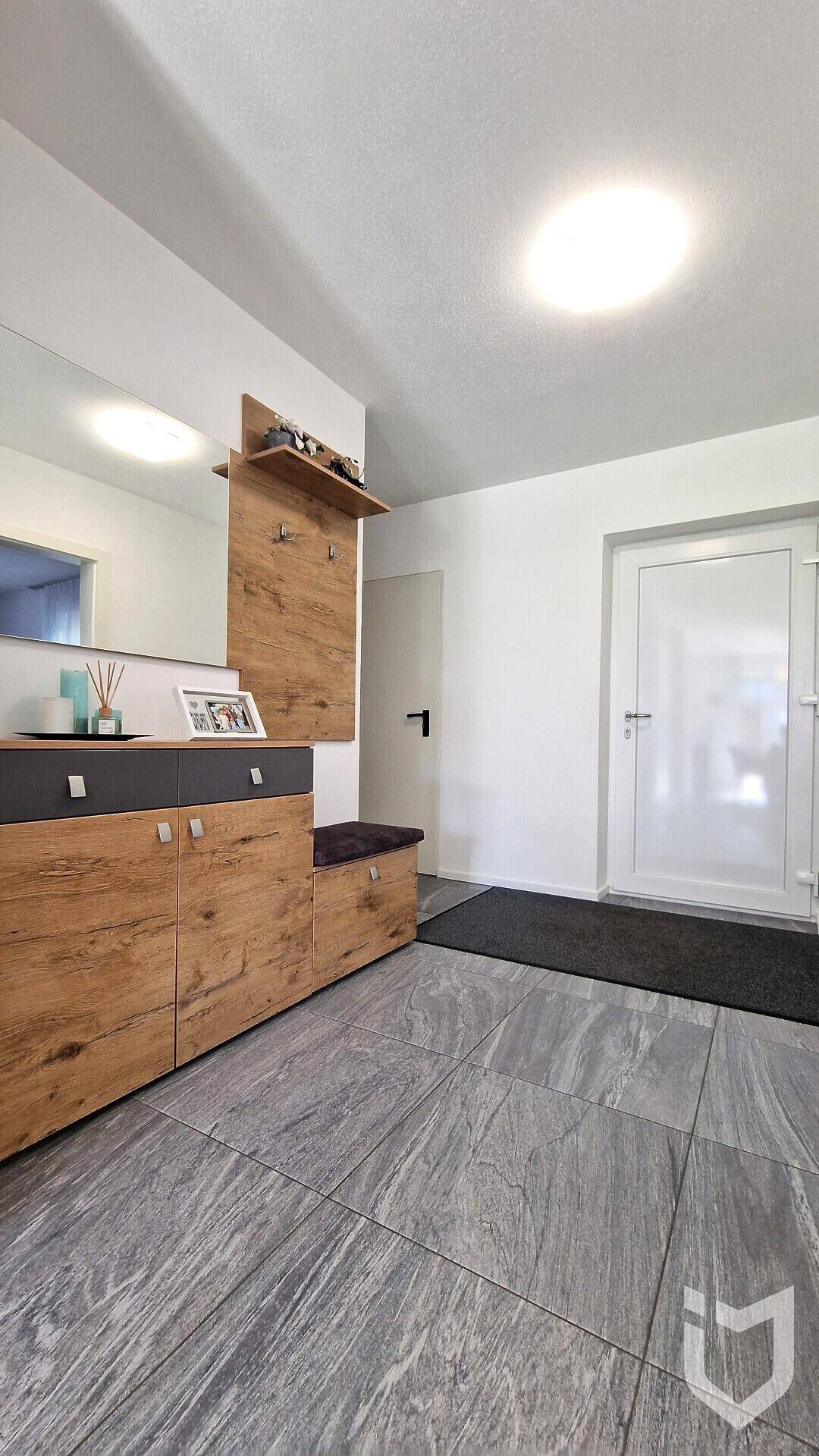 Heller Eingangsbereich mit modernen Holzmöbeln und großformatigen Fliesen.