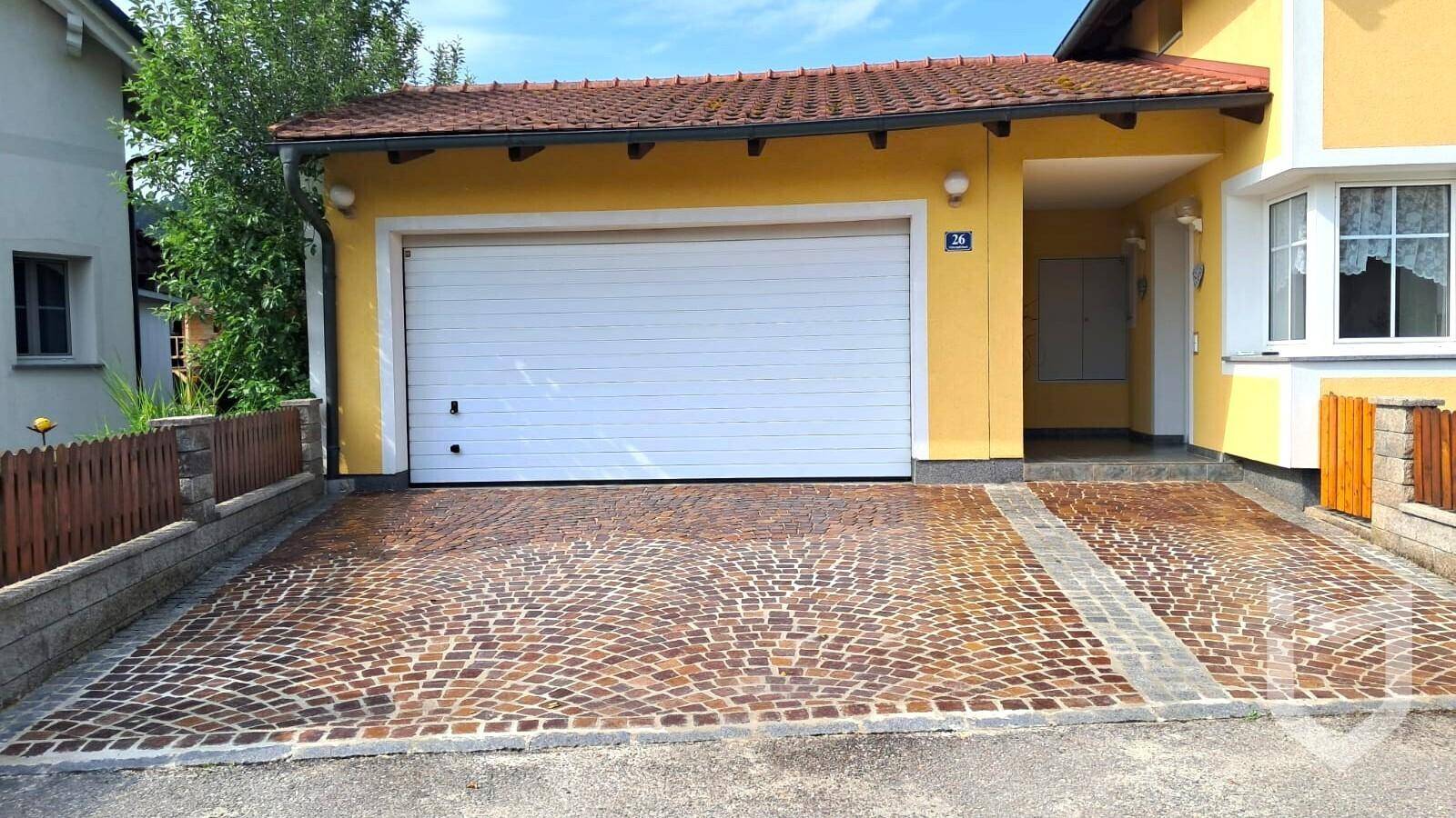 Vorderansicht des Hauses mit gepflasterter Einfahrt und integrierter Garage.