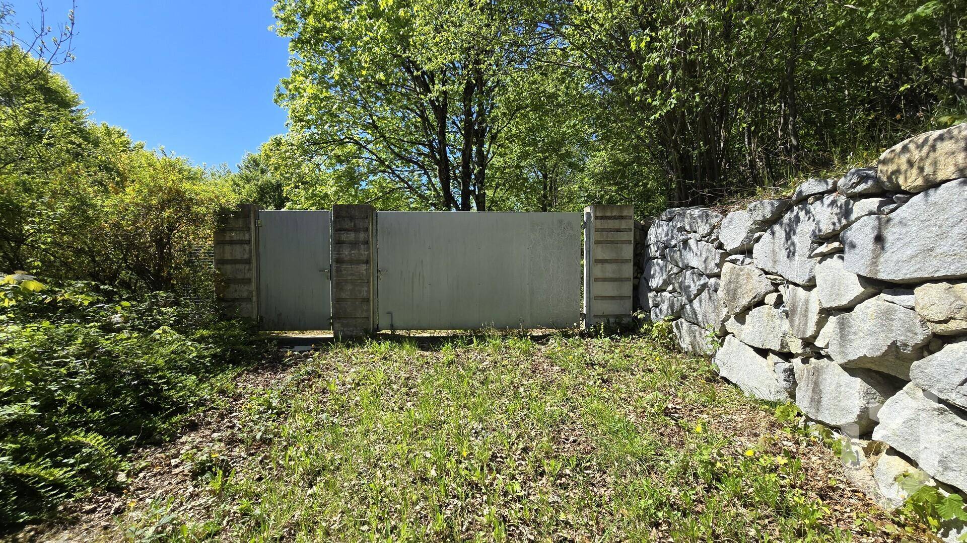 Natursteinmauer und ein Tor, die einen Teil des Grundstücks abgrenzen und Privatsphäre bieten.