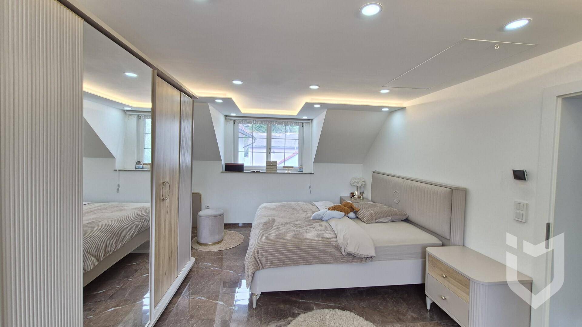 Gemütliches Schlafzimmer im Dachgeschoss mit Bett, Kleiderschrank und indirekter Beleuchtung.