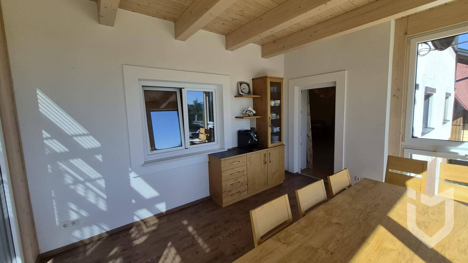 Heller Wintergarten mit Holzbalkendecke und Holzboden, ausgestattet mit einem Sideboard und Blick ins Grüne.