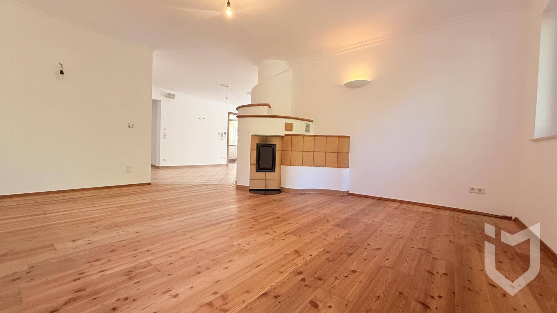 Geräumiges Wohnzimmer mit Holzdielenboden und einem traditionellen Kachelofen als Heizelement.