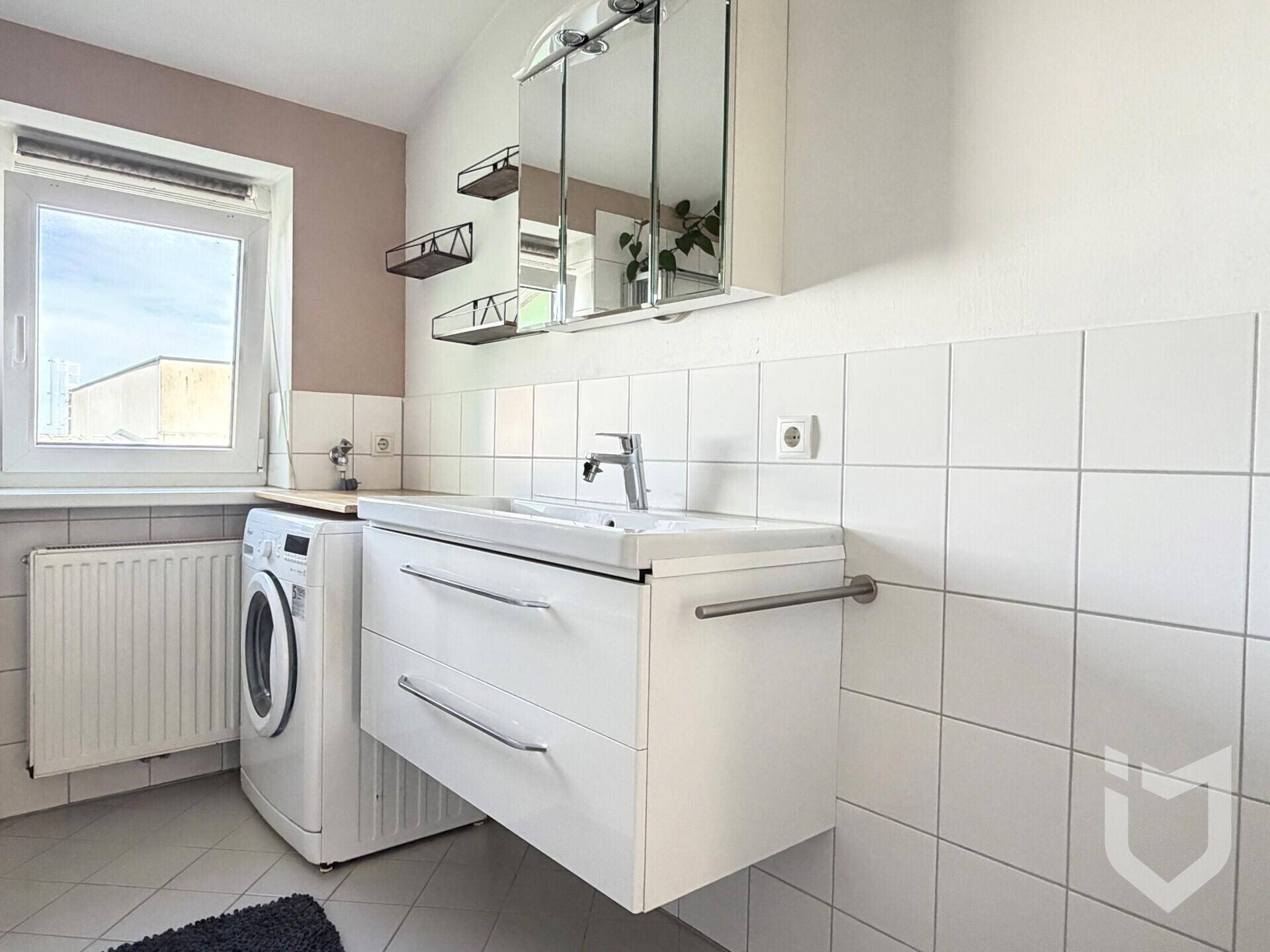 Modernes Badezimmer mit Waschbecken, Spiegelschrank, Waschmaschine und Fenster.