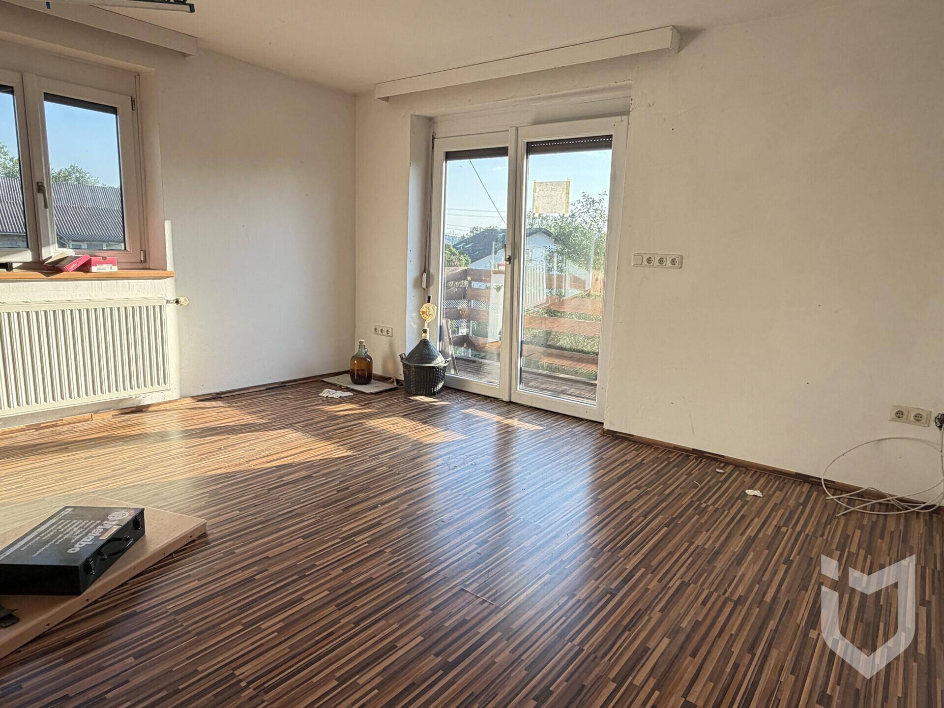 Heller Wohnraum mit Laminatboden und Zugang zu einem Balkon oder einer Terrasse.