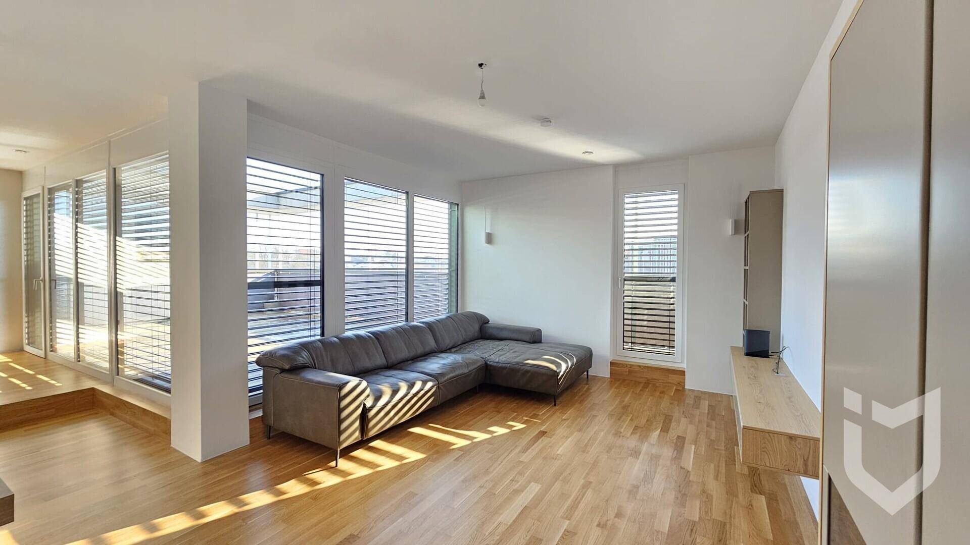 Großzügiges Wohnzimmer mit L-förmigem Sofa, Holzboden und bodentiefen Fenstern für viel Tageslicht.