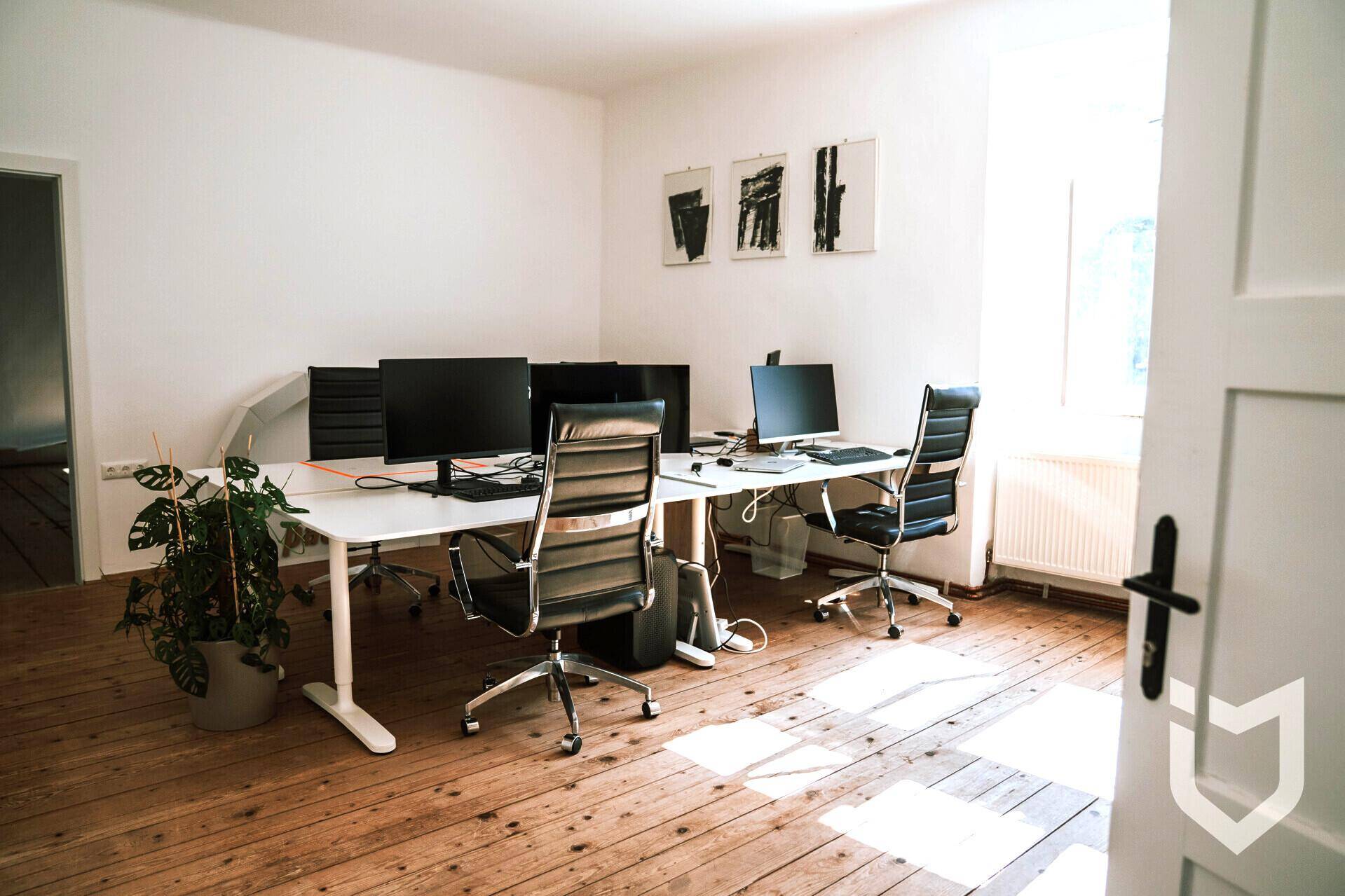 Geräumiger Büroraum mit mehreren Schreibtischen, ergonomischen Stühlen und Holzdielenboden.