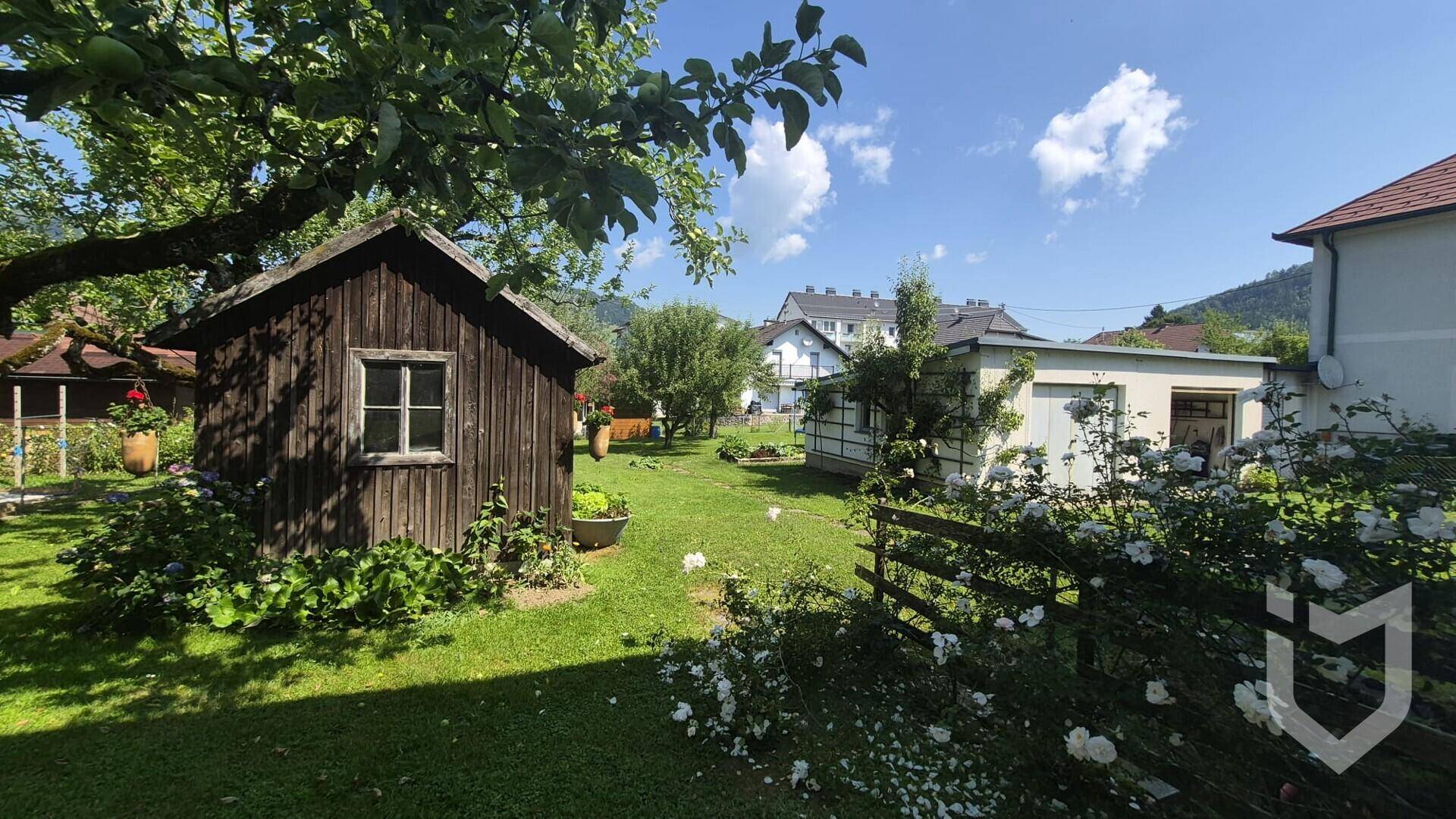 Gepflegter Garten mit einem rustikalen Holzschuppen, Rasen und blühenden Pflanzen.