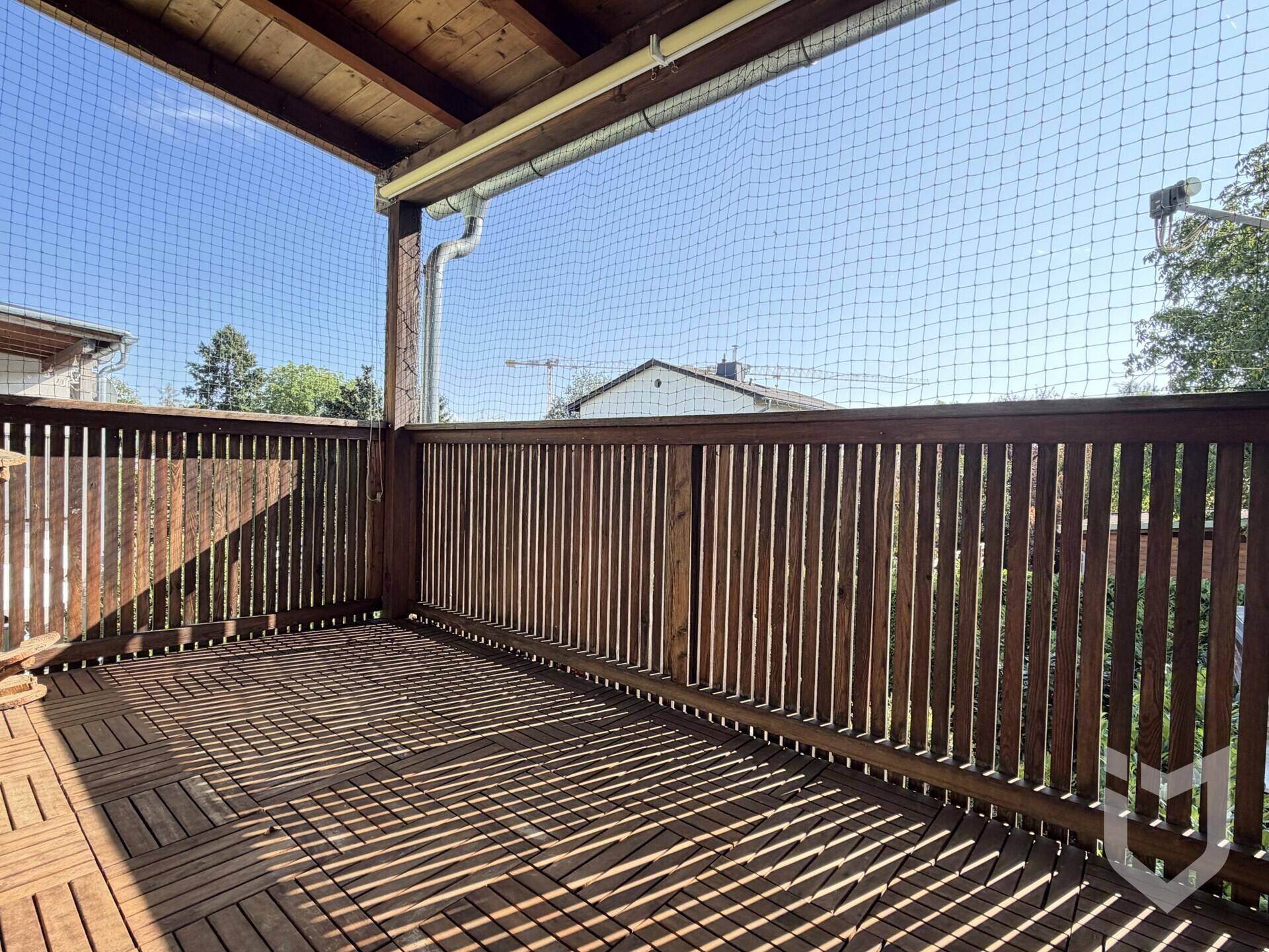 Überdachter Balkon mit Holzboden und Holzgeländer, gesichert durch ein Schutznetz.