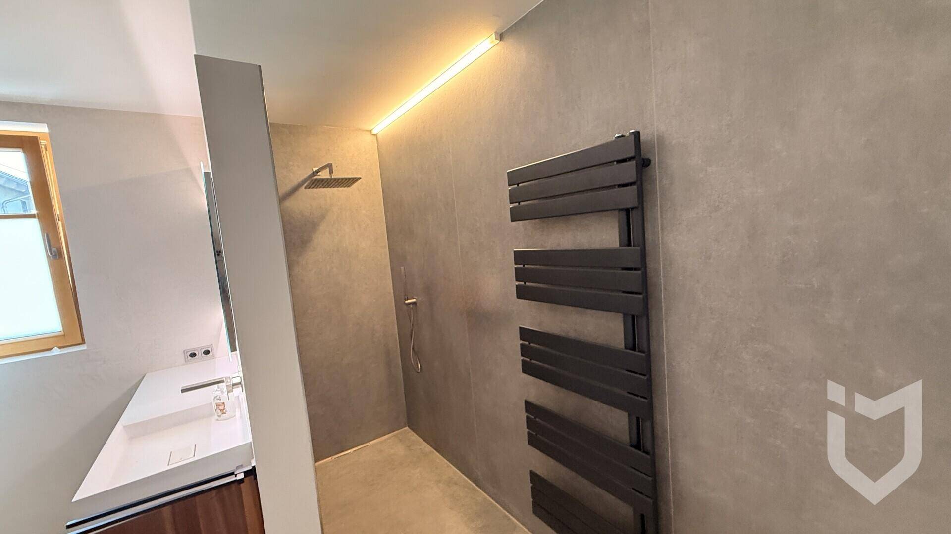 Moderne Duschkabine mit Regendusche, grauen Fliesen und praktischem Handtuchheizkörper.