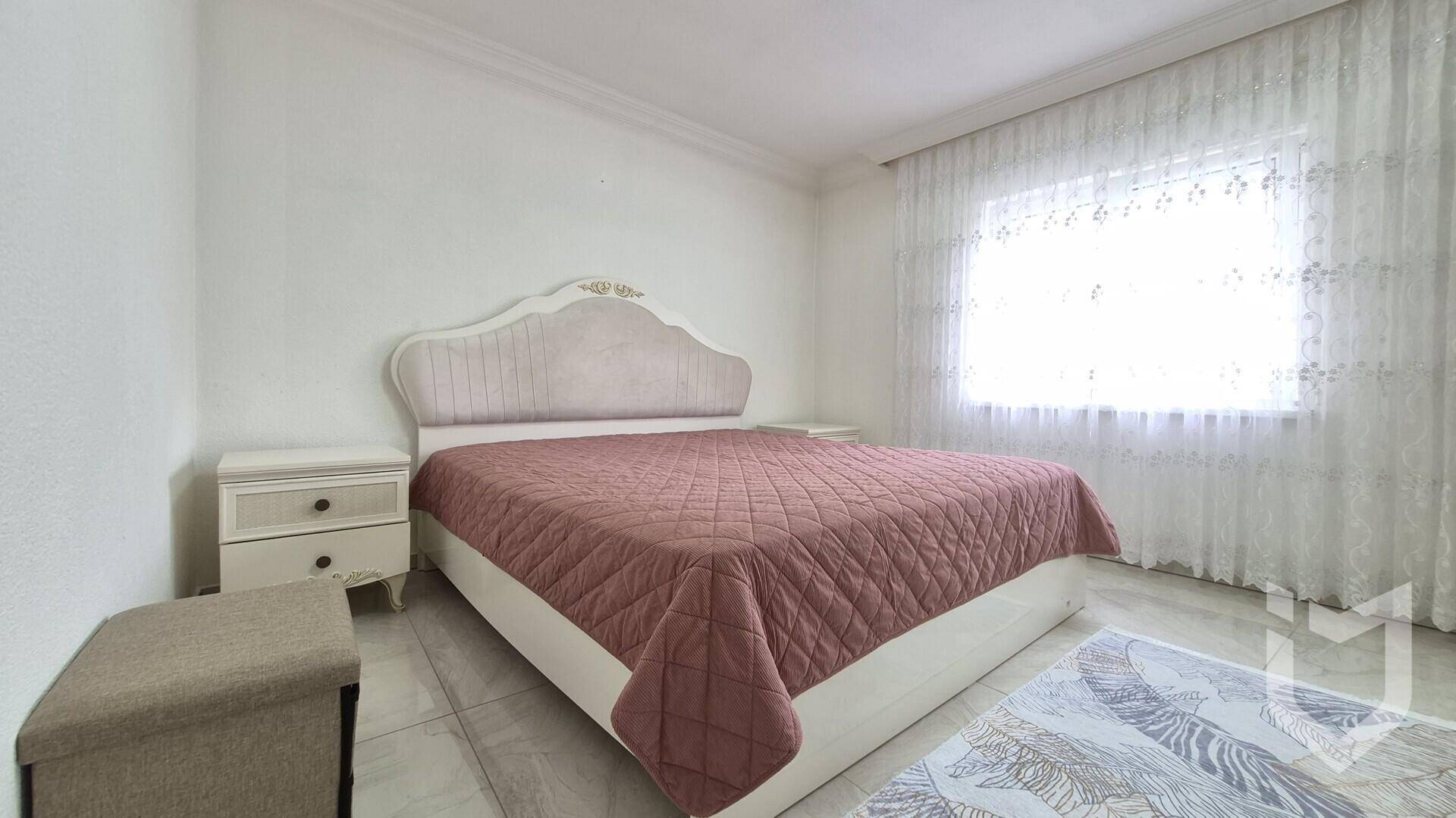 Helles Schlafzimmer mit großem Bett, Nachttischen und einem Fenster mit Vorhängen.