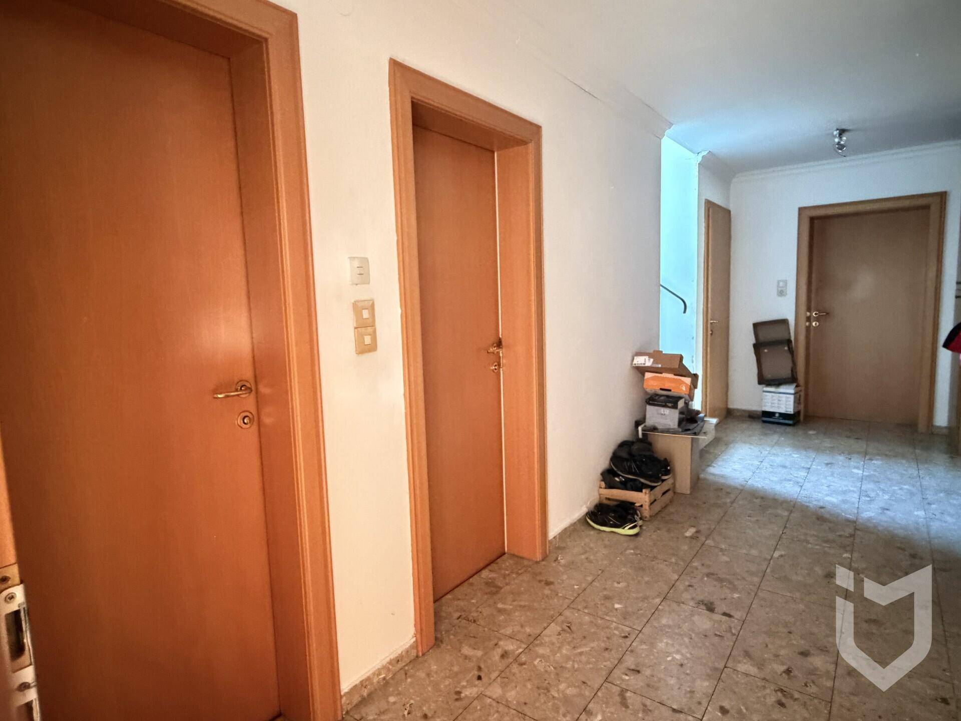 Langer Flur mit mehreren Holztüren und Terrazzoboden, der zu den Zimmern führt.