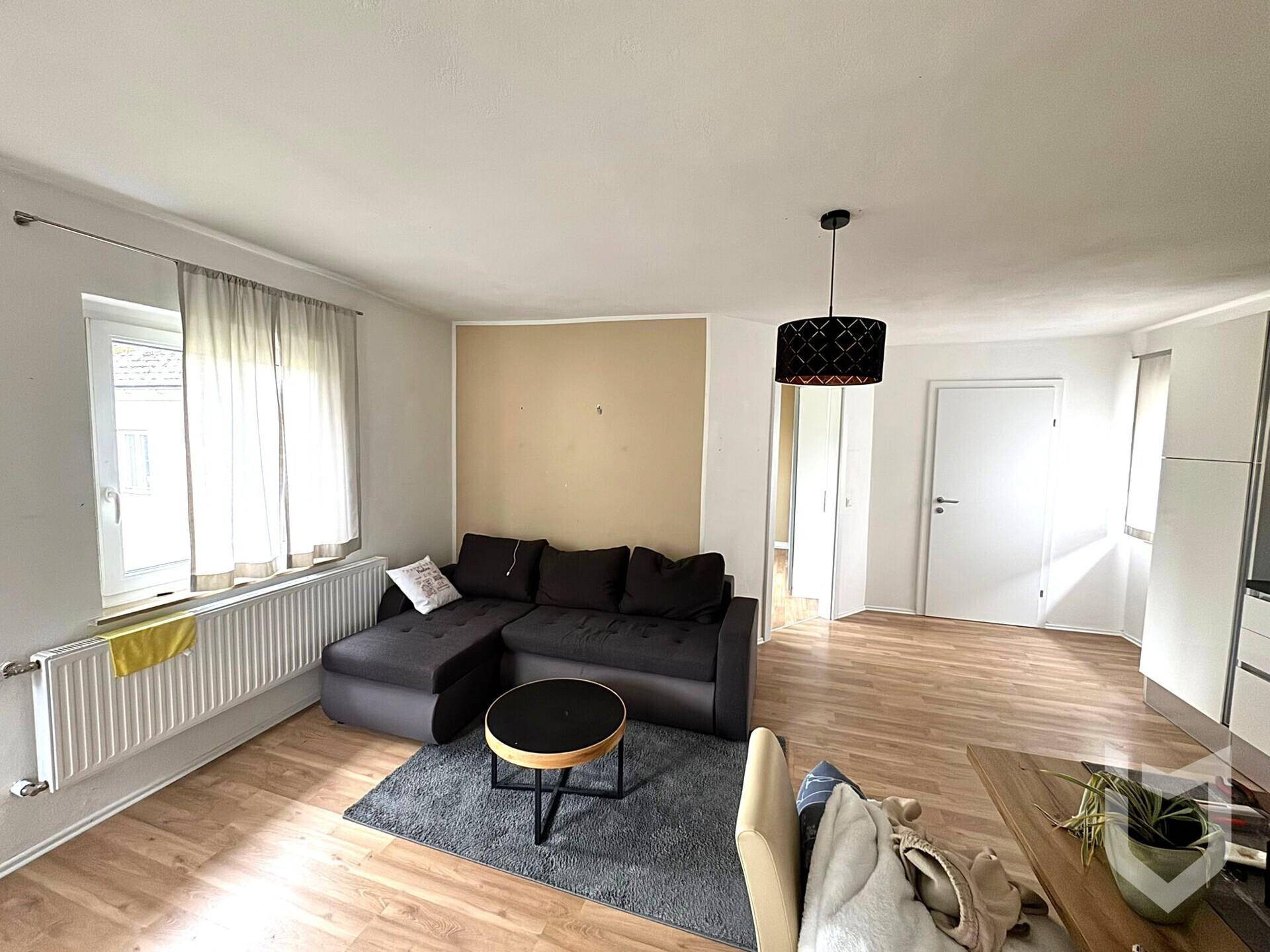 Helles Wohnzimmer mit dunklem Ecksofa, Teppich und modernem Deckenlicht.