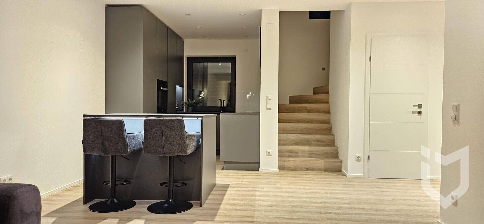 Offener Wohnbereich mit Kücheninsel und Treppe, die in die obere Etage führt.