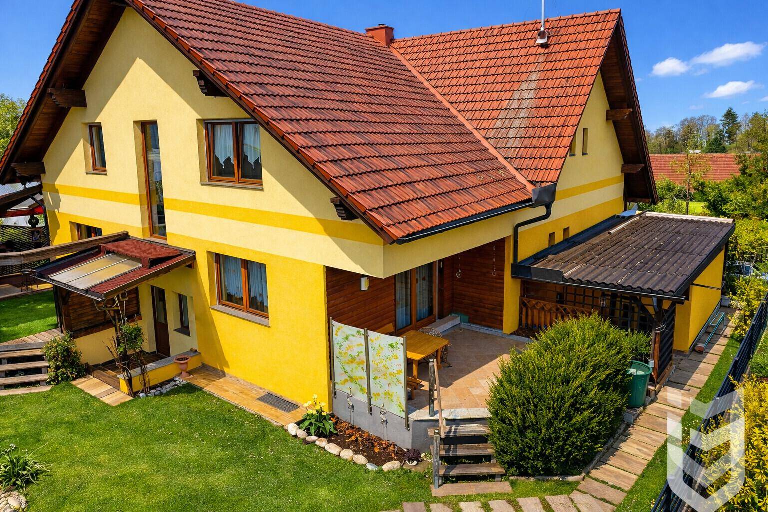 Seitenansicht des Hauses mit einer kleinen gepflasterten Terrasse und angrenzendem grünen Gartenbereich.