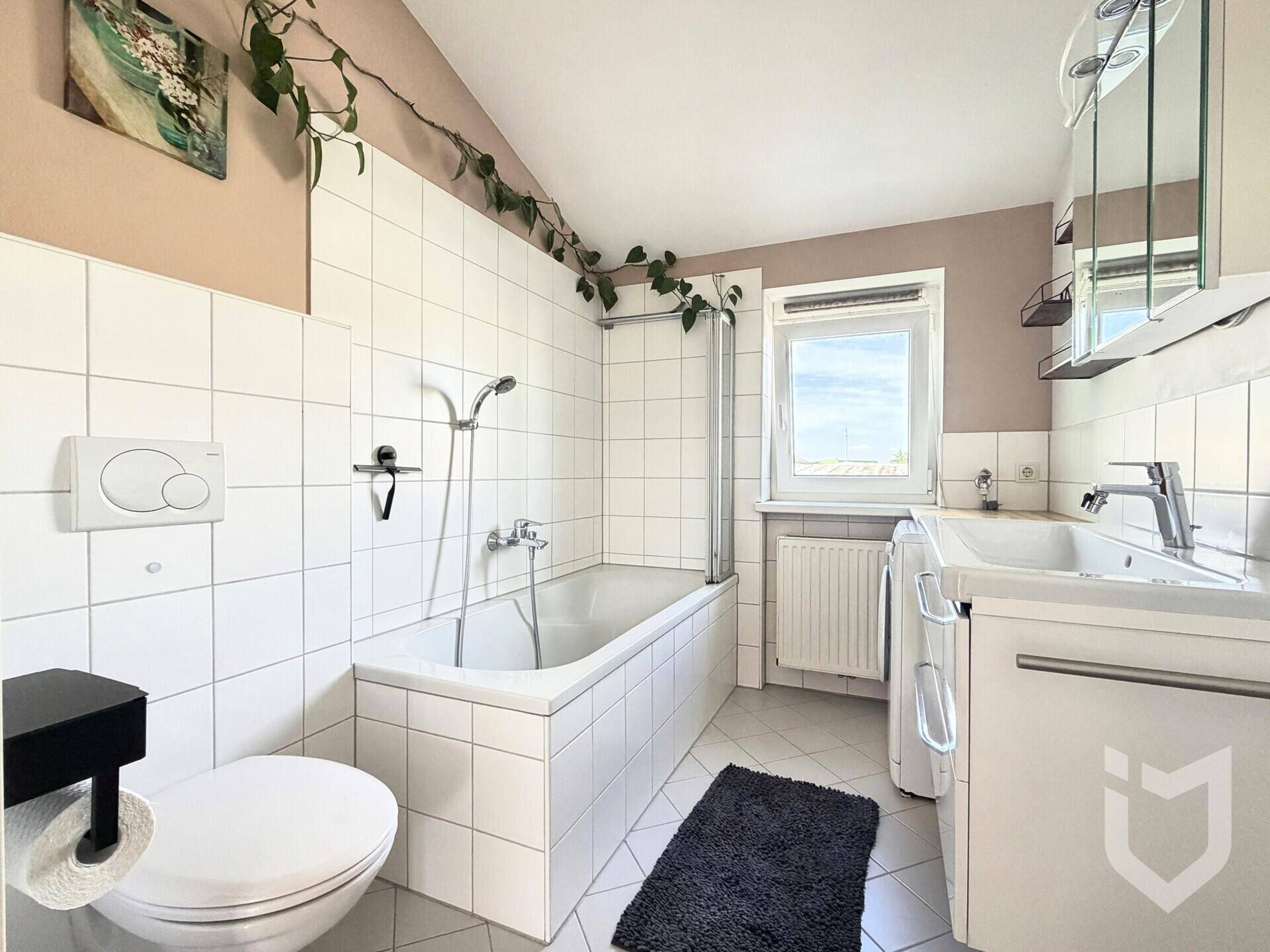 Badezimmer mit Badewanne, WC, Waschbecken, weißen Fliesen und einem Fenster für Tageslicht.