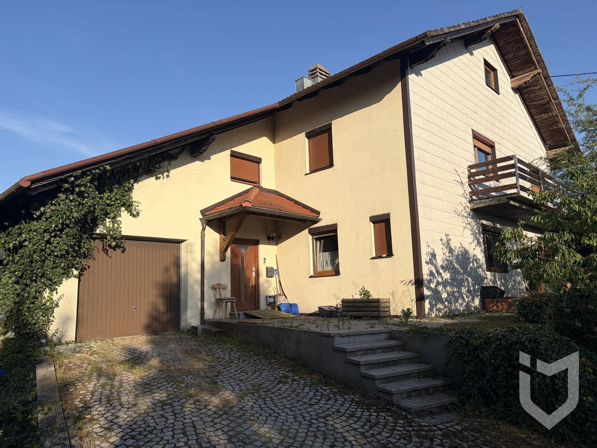 Einfamilienhaus mit Garage, gepflasterter Auffahrt und Eingangsbereich unter blauem Himmel.