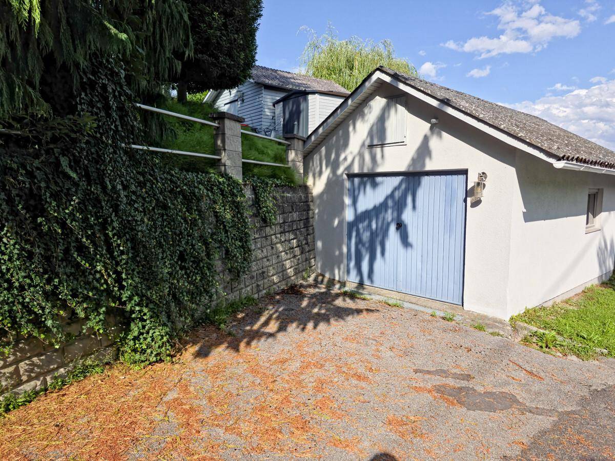 Freistehende Garage mit blauem Tor und Zufahrt, umgeben von Grün.