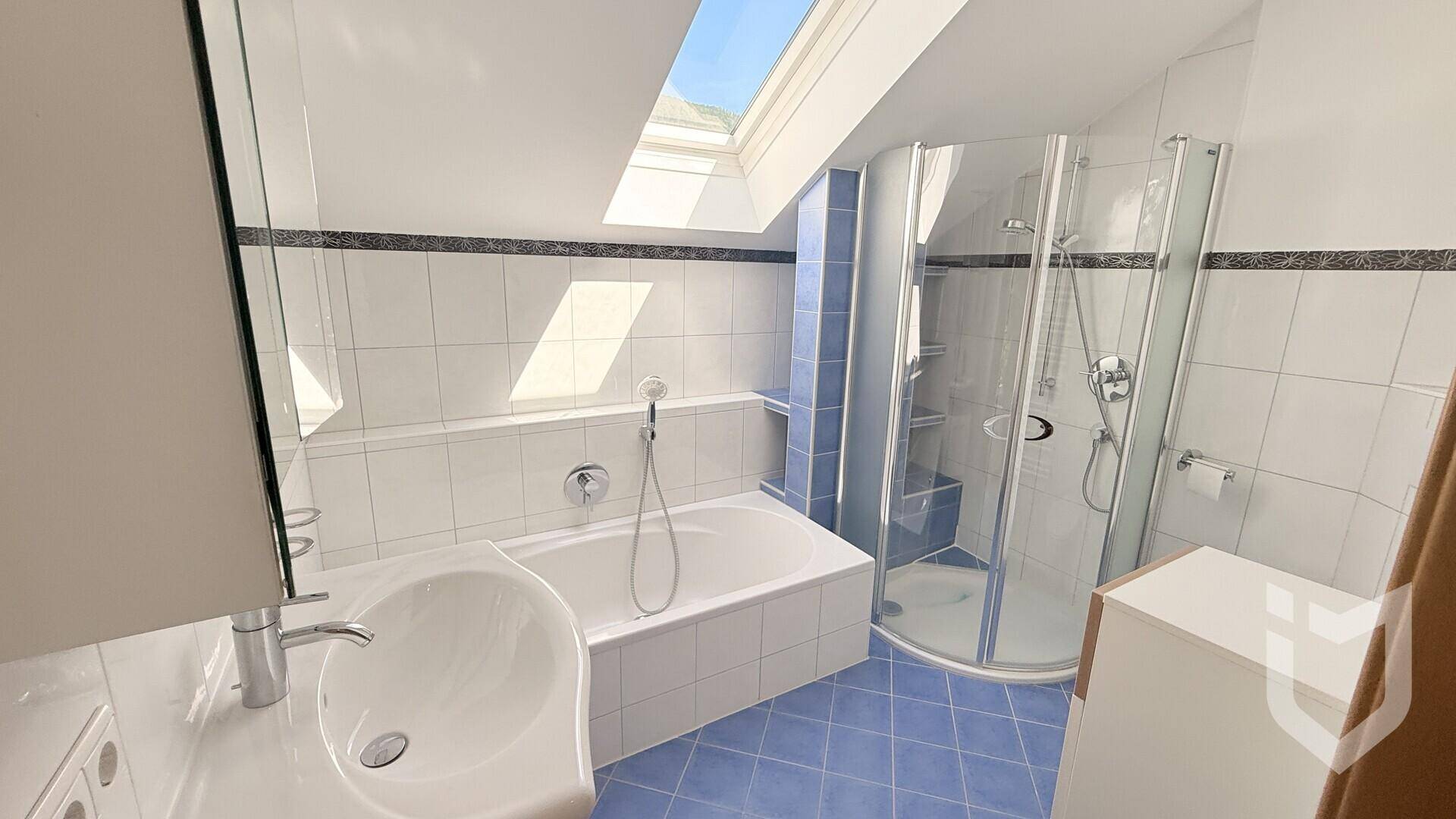 Helles Badezimmer mit Badewanne, Eckdusche, Einzelwaschbecken und Dachfenster.