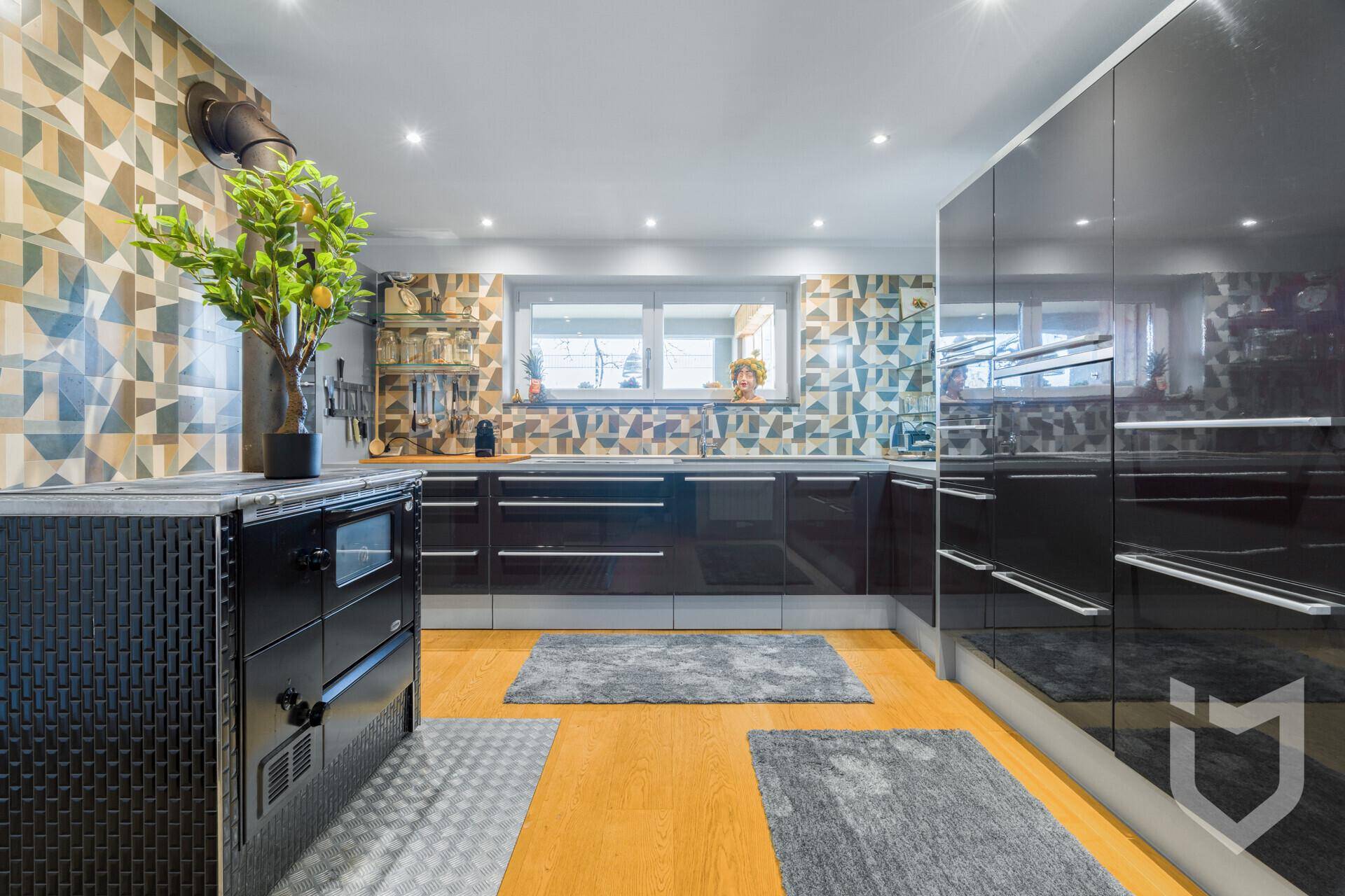 Moderne Küche mit schwarzen Hochglanzfronten, Holzboden und gemusterter Wandfliese.