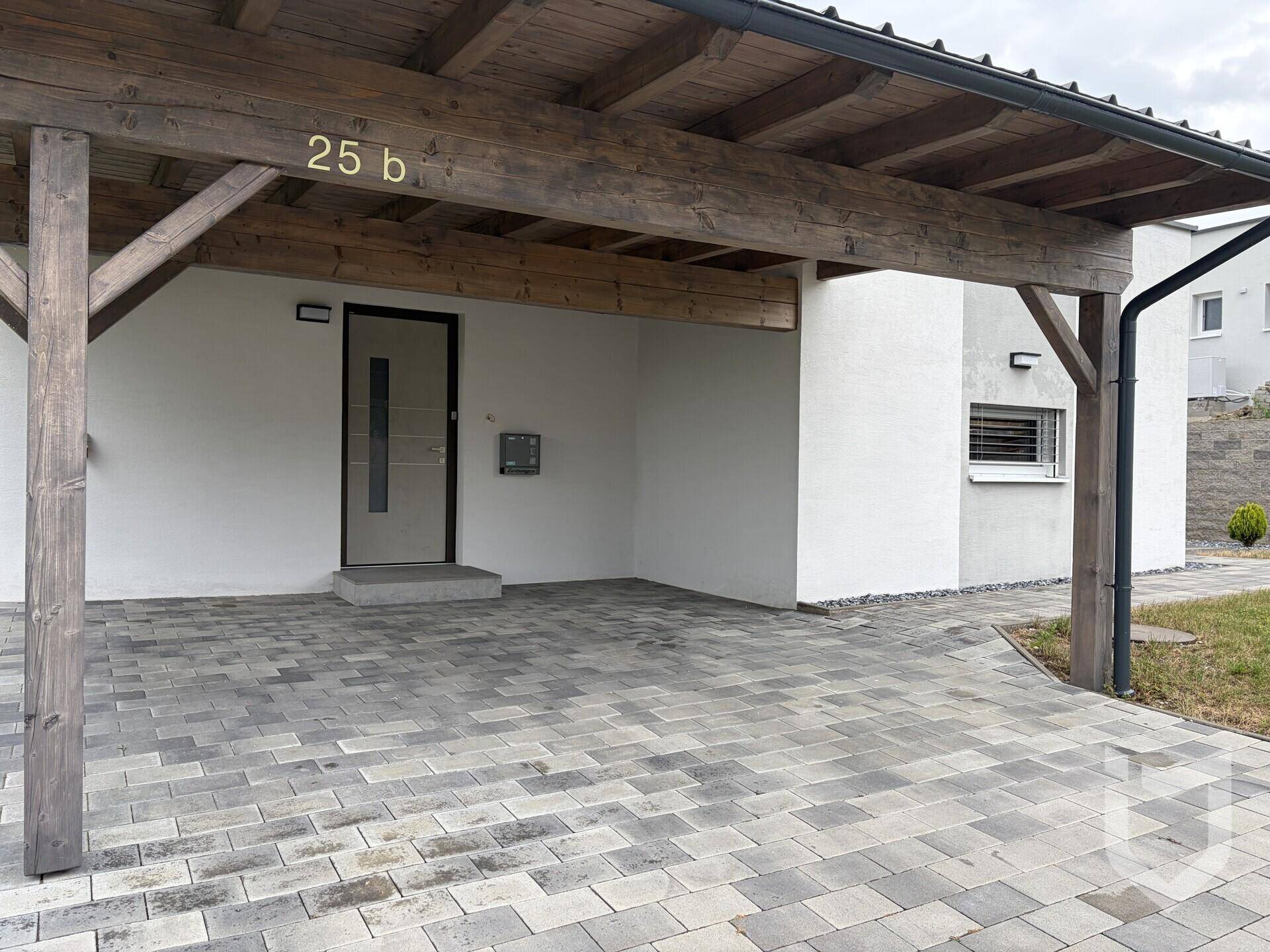 Eingangsbereich des Hauses mit überdachtem Carport und gepflasterter Zufahrt.