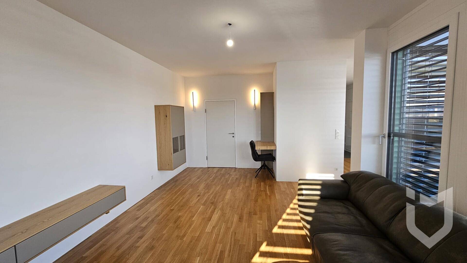 Helles Wohnzimmer mit Holzboden, bietet Platz für einen Arbeitsbereich und Zugang zu weiteren Räumen.