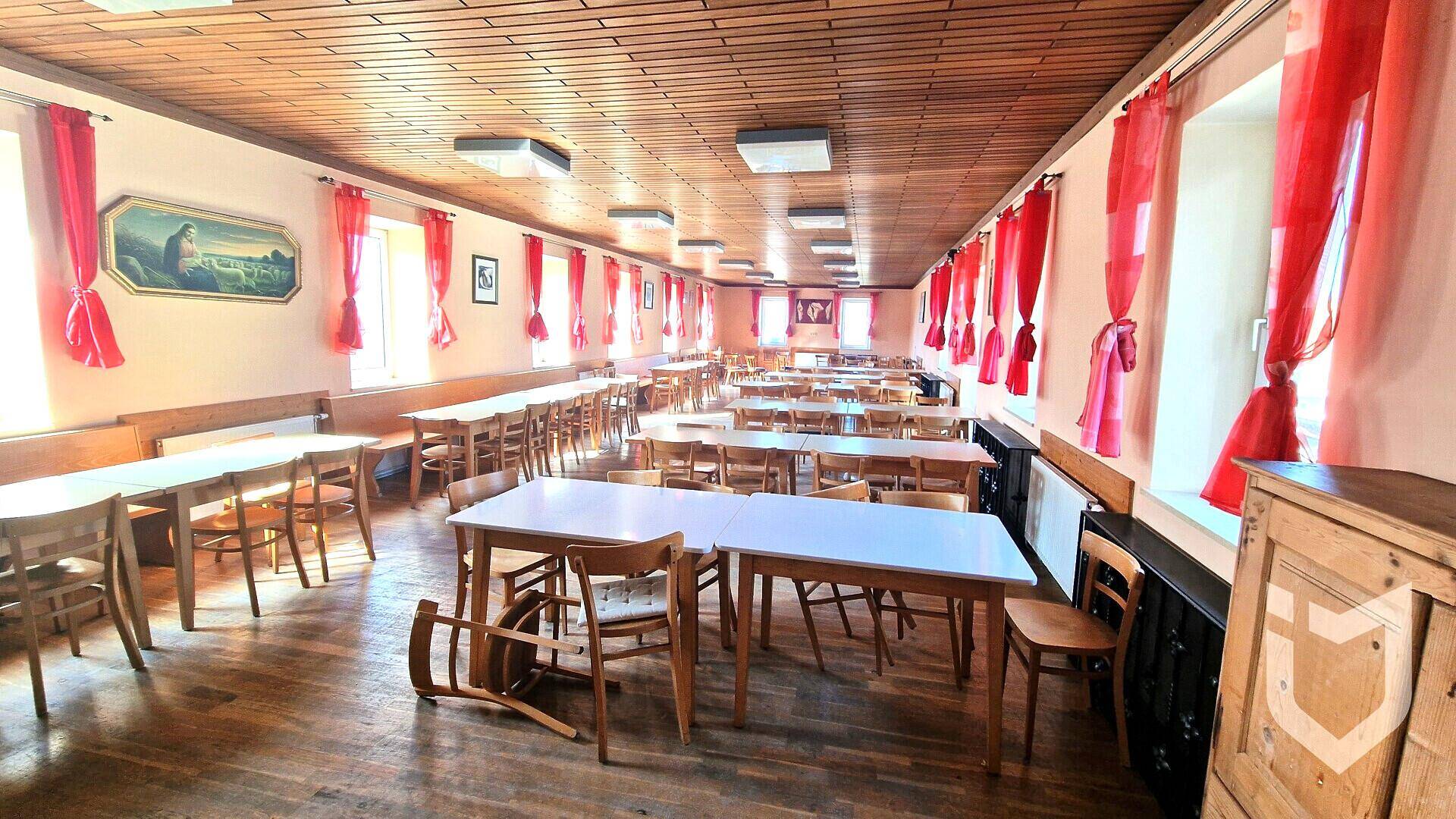 Großer Speisesaal mit vielen Tischen, Holzdecken und roten Vorhängen.