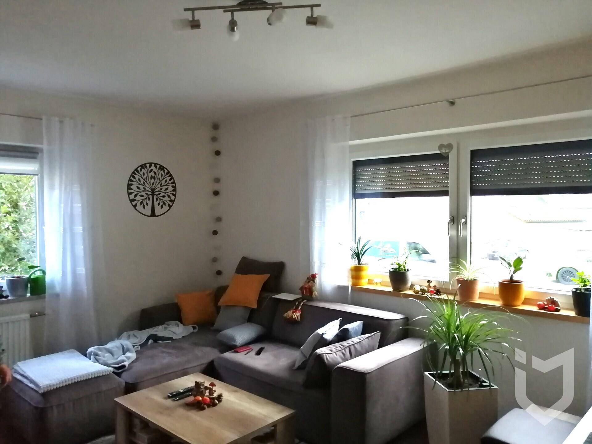 Helles Wohnzimmer mit großem Ecksofa, Couchtisch und vielen Pflanzen.
