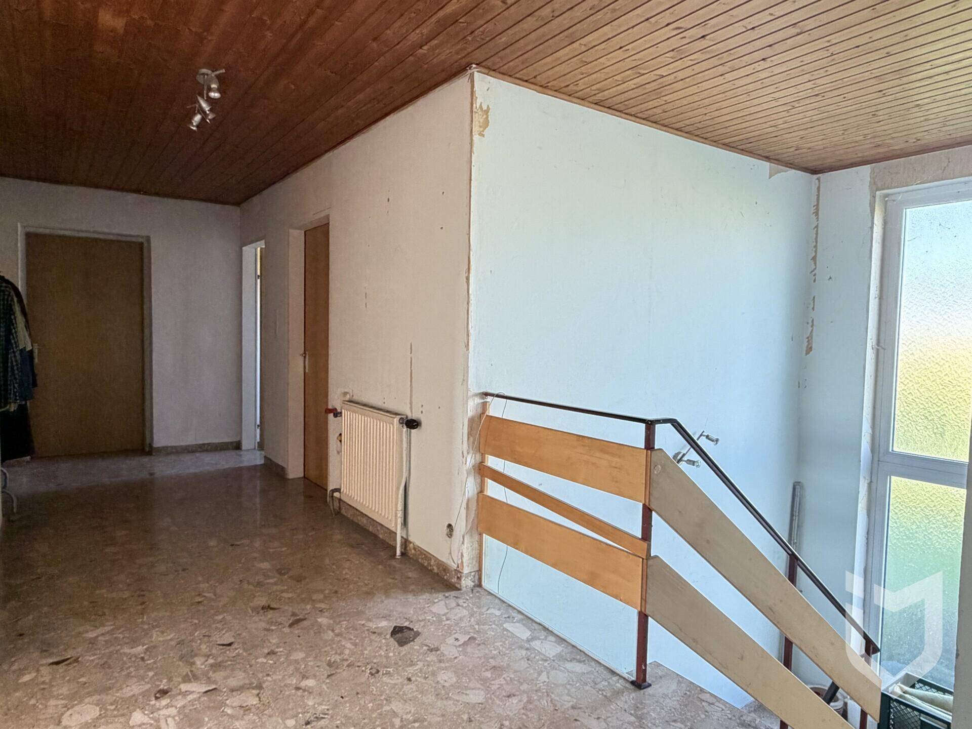 Flur mit Treppenaufgang, Terrazzoboden und Holzdeckenverkleidung, renovierungsbedürftig.