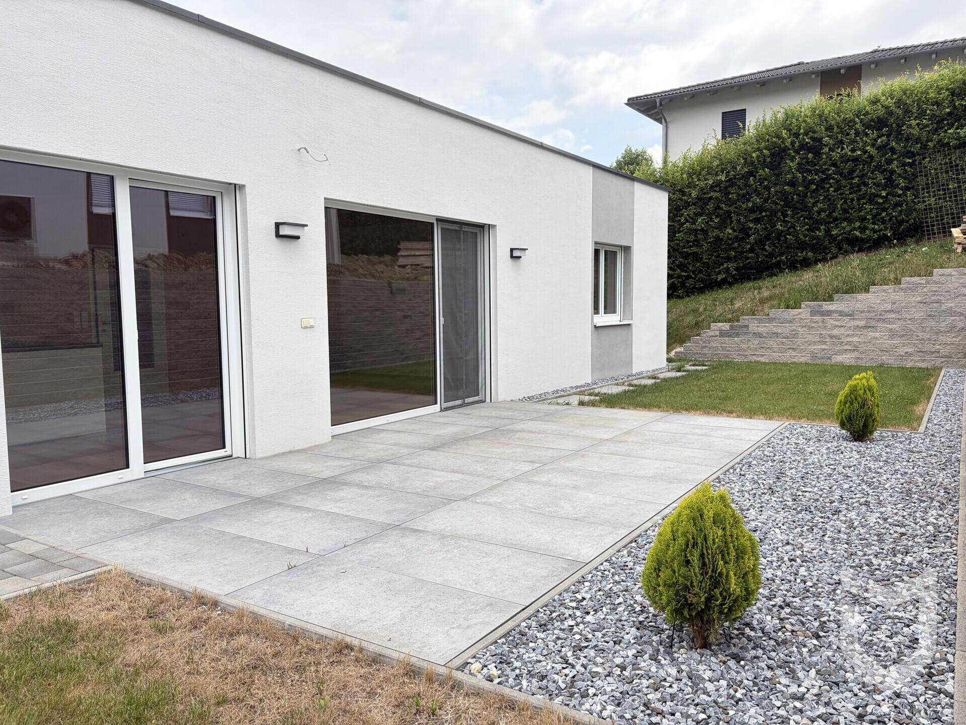 Großzügige Terrasse mit Steinplatten, umgeben von Kies und Rasen, mit Zugang zum Haus.