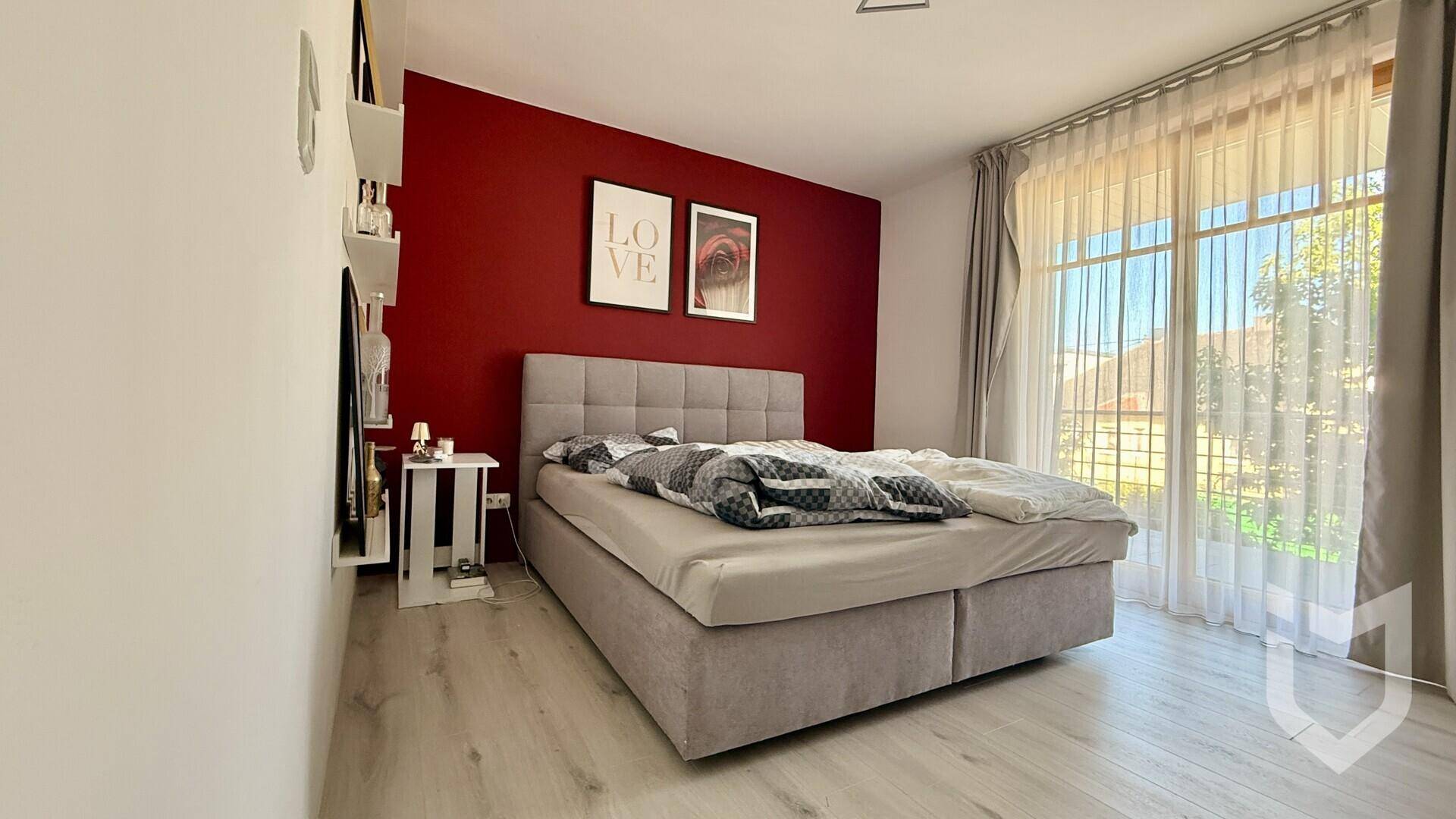 Schlafzimmer mit großem Bett, auffälliger roter Akzentwand und hellem Holzboden.