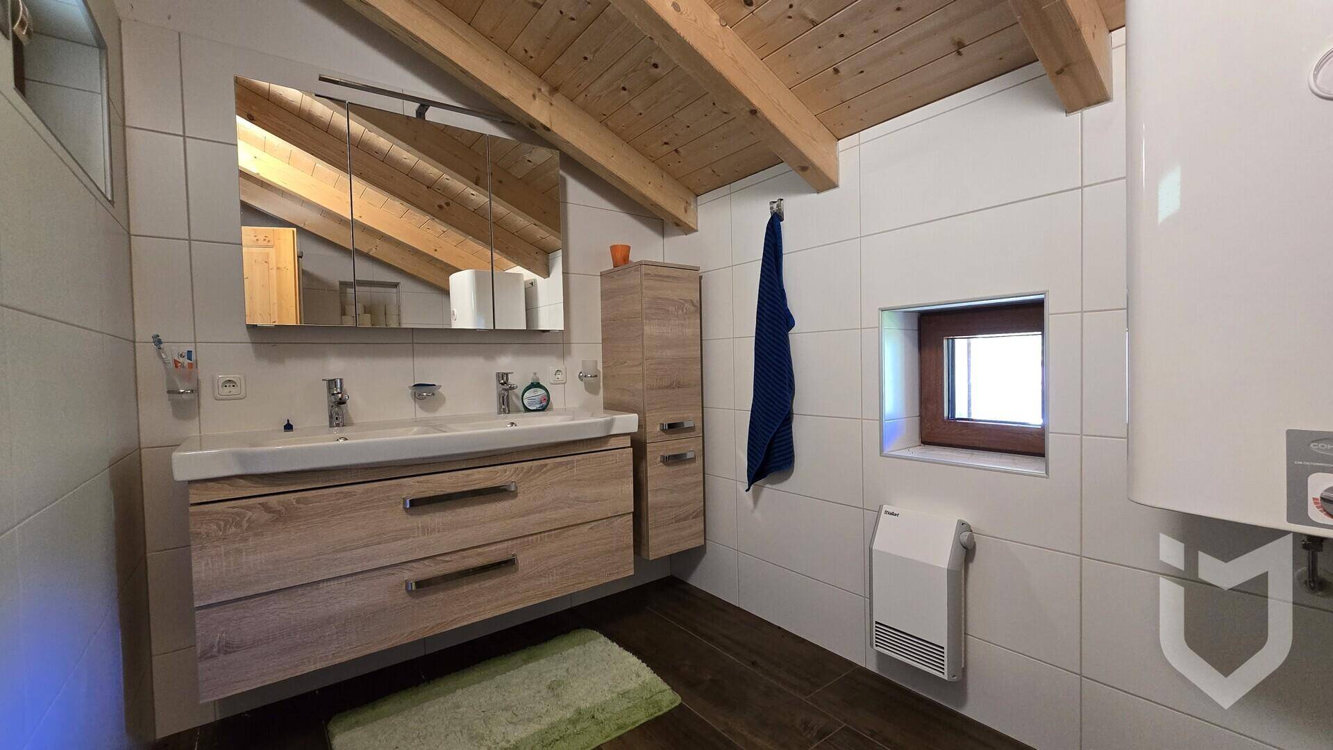 Badezimmer mit Doppelwaschbecken, Spiegelschrank und schräger Holzdecke im Dachgeschoss.