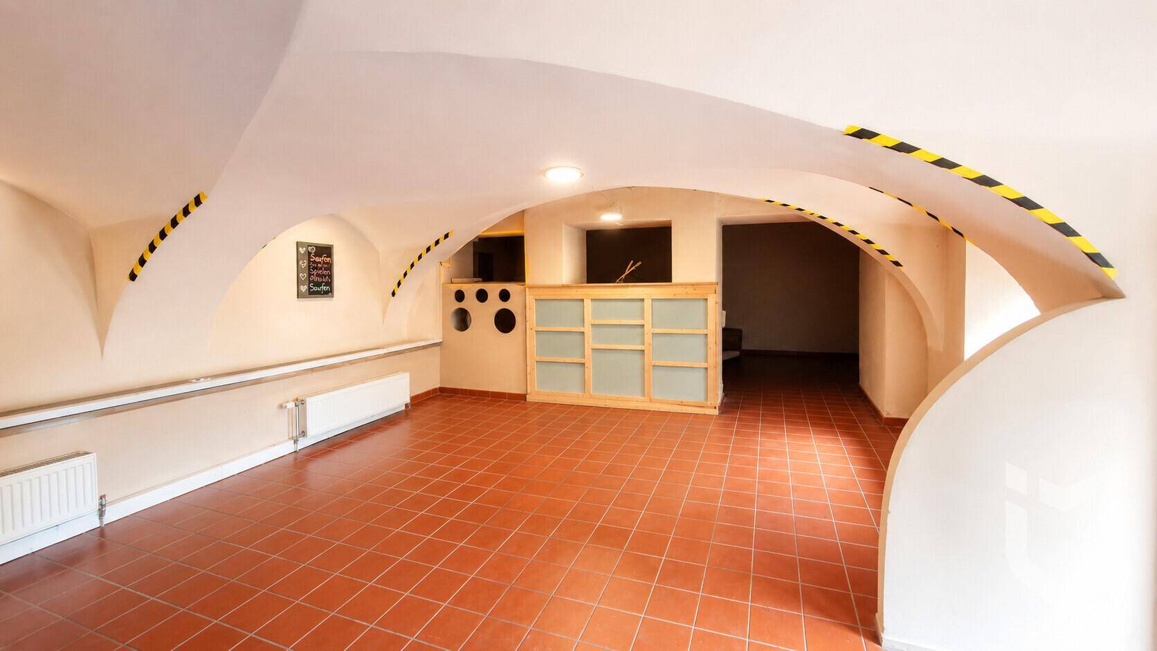 Großer Raum mit Gewölbedecke und Terrakottafliesenboden, möglicherweise ein Kellerraum.