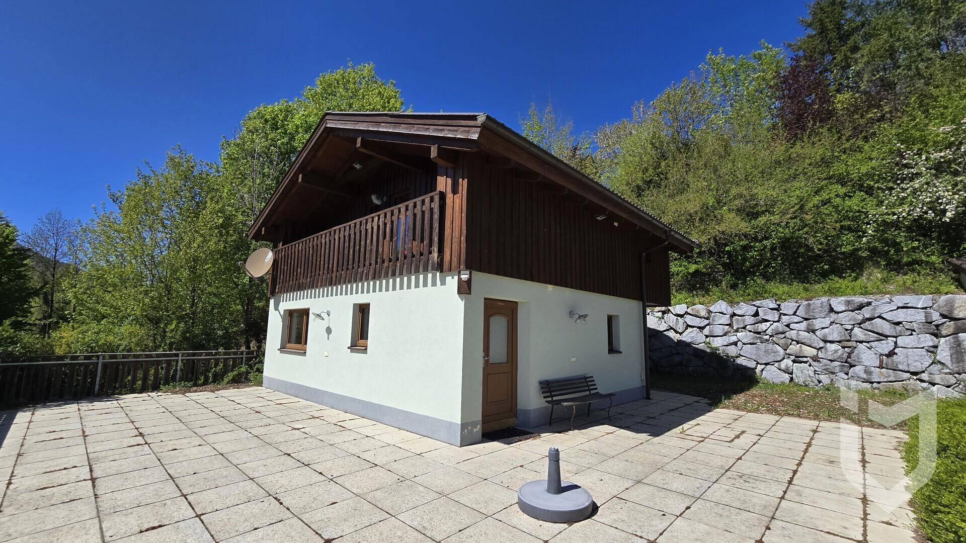 Hausansicht mit großer gepflasterter Fläche vor dem Eingang und einer Natursteinmauer seitlich des Gebäudes.