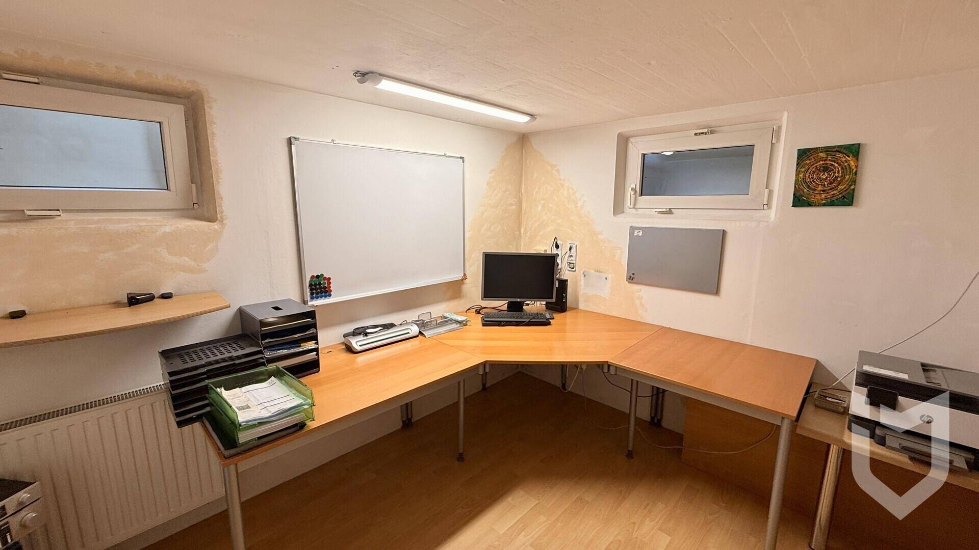 Funktionales Büro im Untergeschoss mit großem Eckschreibtisch und kleinen Fenstern für Tageslicht.
