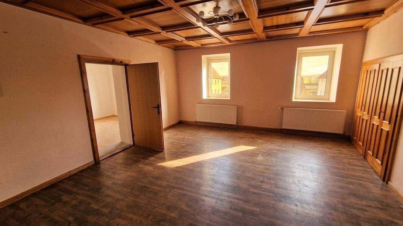 Geräumiger Raum mit Holzkassettendecke, zwei Fenstern und Holzboden.