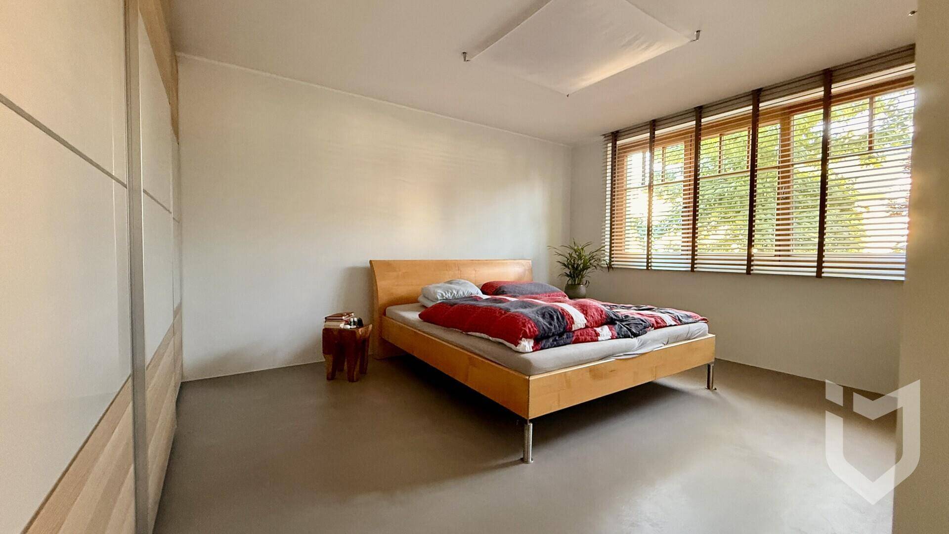 Schlafzimmer mit hellem Holzbett, großzügigen Fenstern und praktischen Jalousien für Privatsphäre.