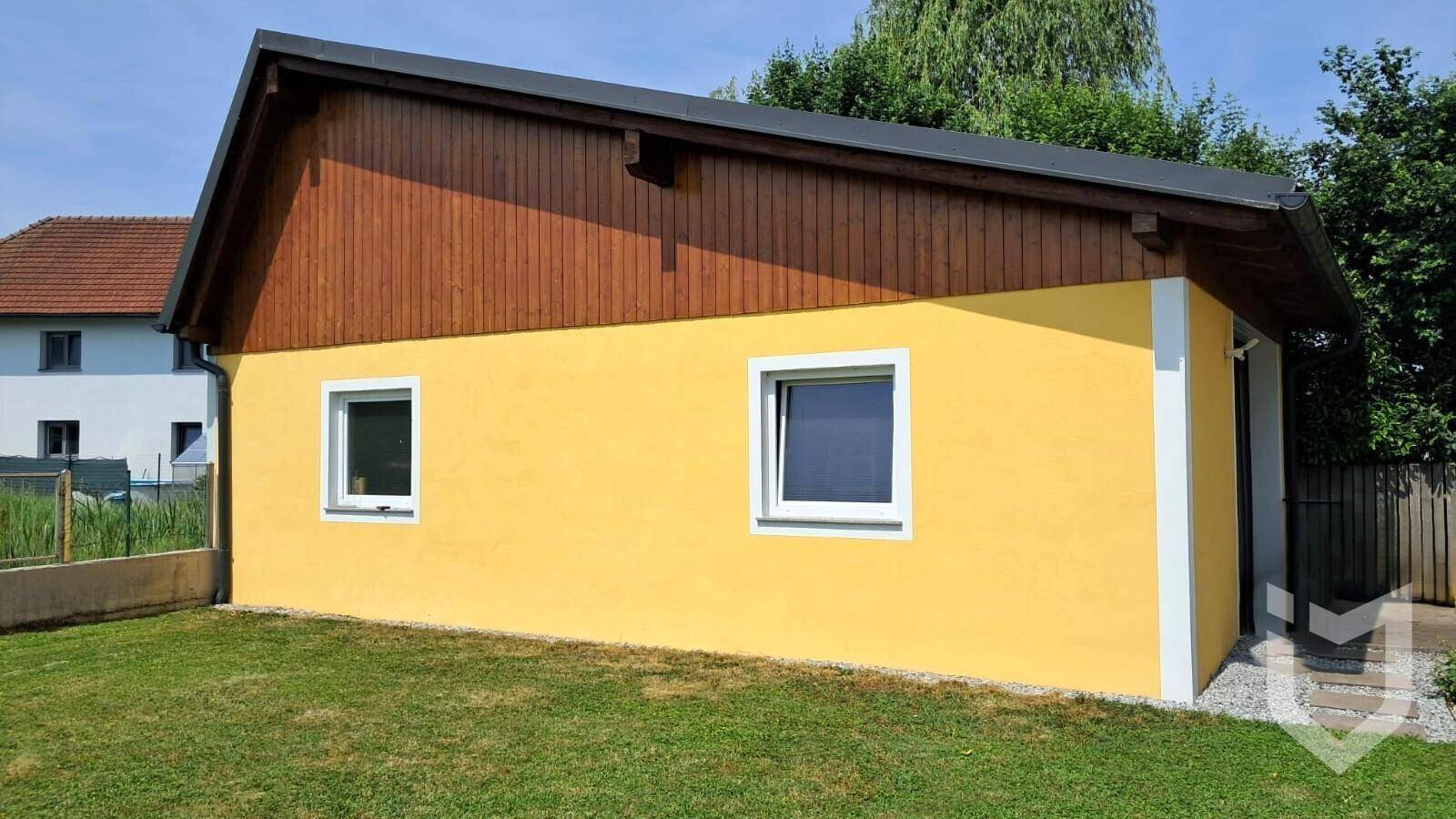 Seitenansicht eines Nebengebäudes mit gelber Fassade und Holzverkleidung im oberen Bereich.