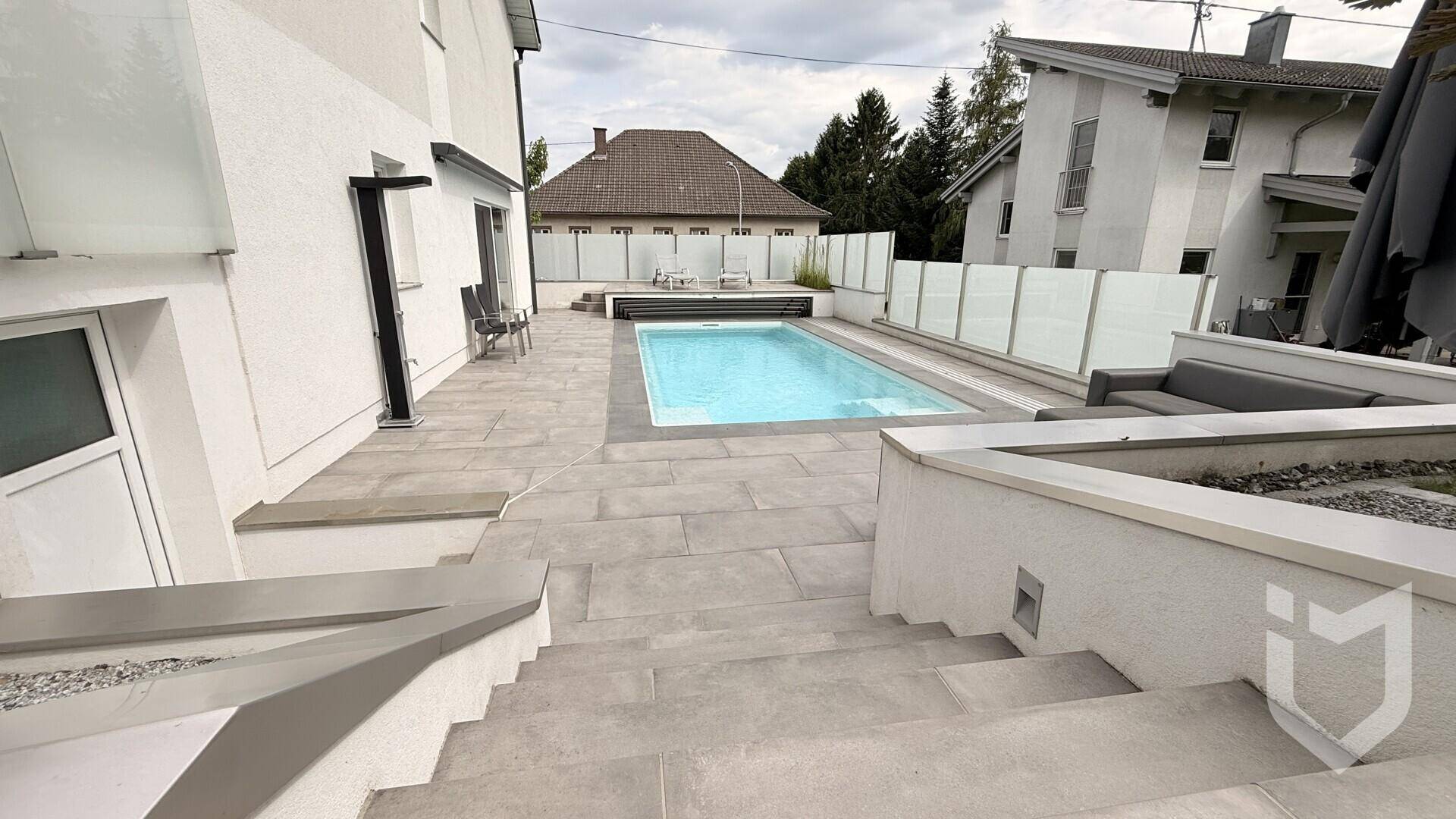Großzügige Terrasse mit modernen Fliesen und Treppen, die zum erfrischenden Poolbereich führen.