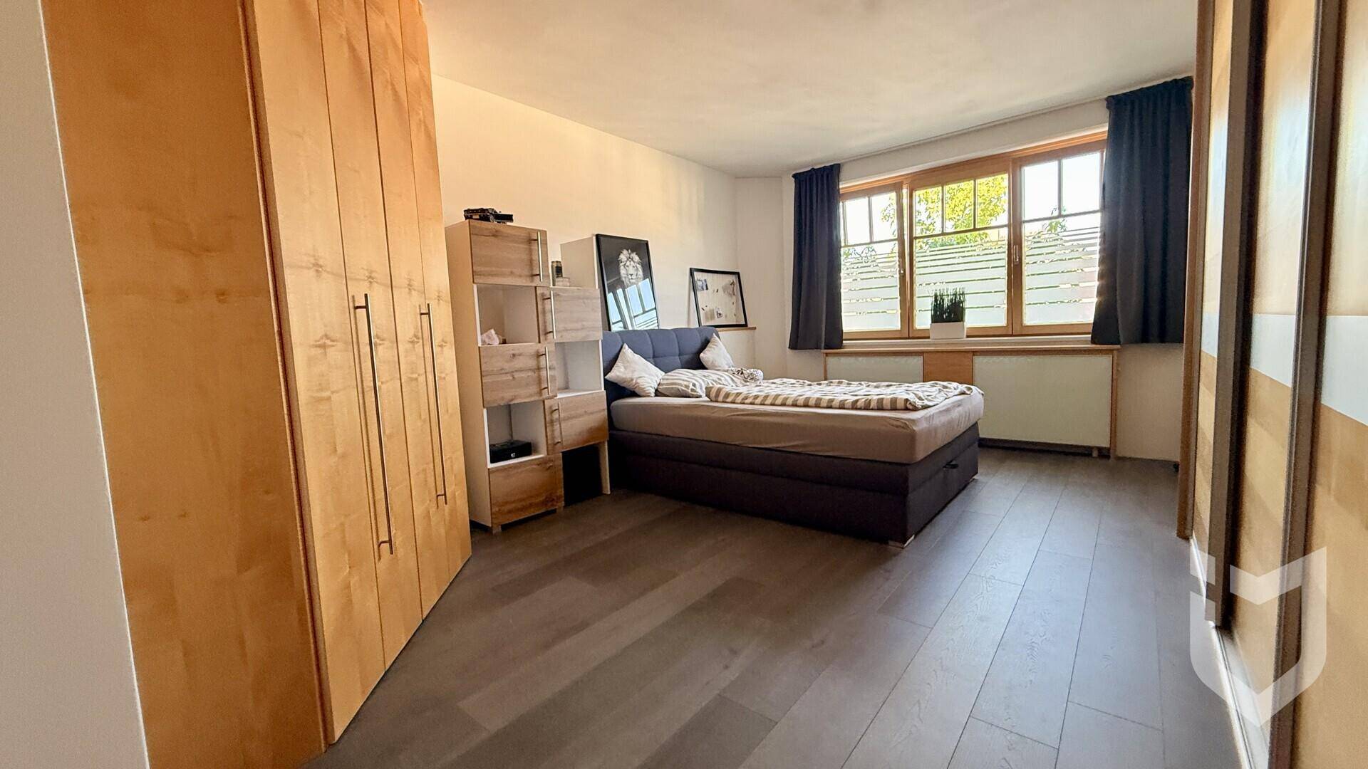 Schlafzimmer mit Bett, großen Holzschränken und dunklem Holzboden, gut beleuchtet.