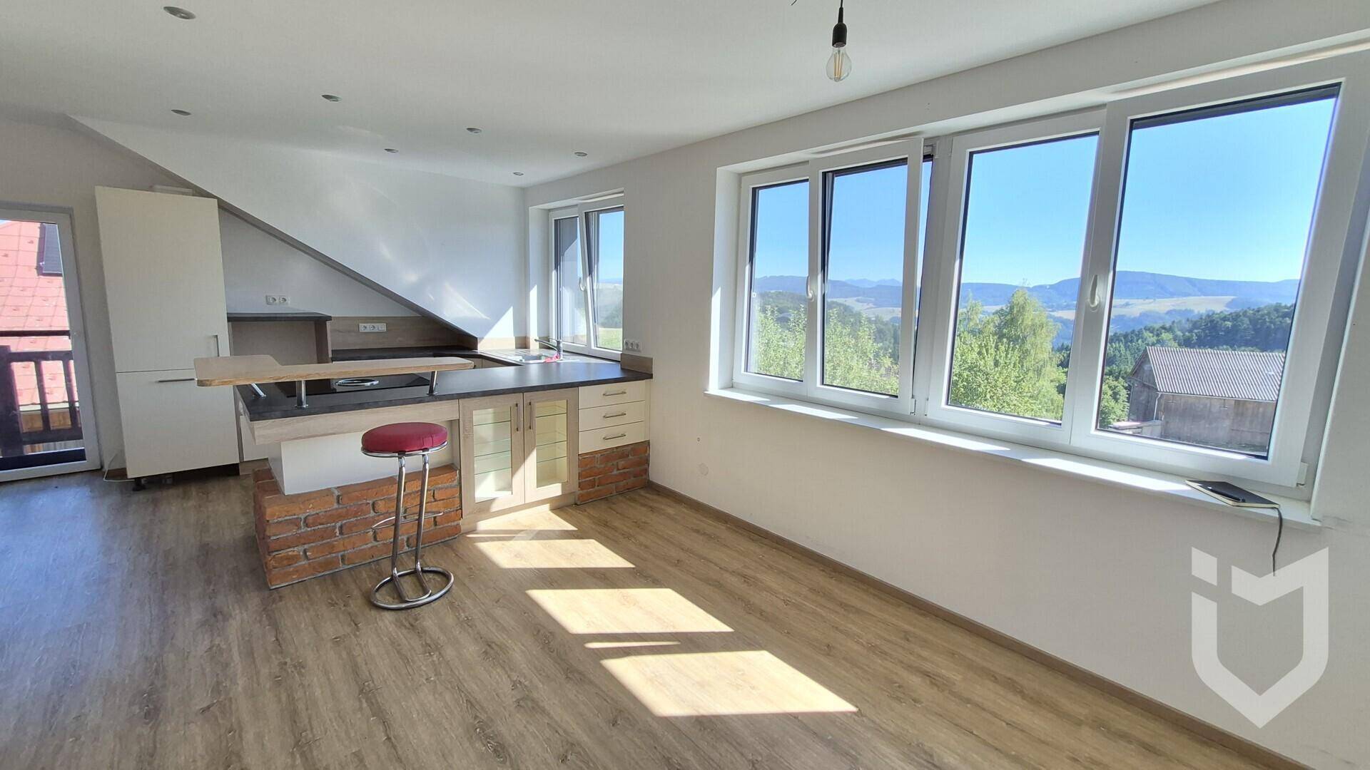 Heller Wohnbereich mit offener Küche, Dachschräge und großen Fenstern mit Bergblick.