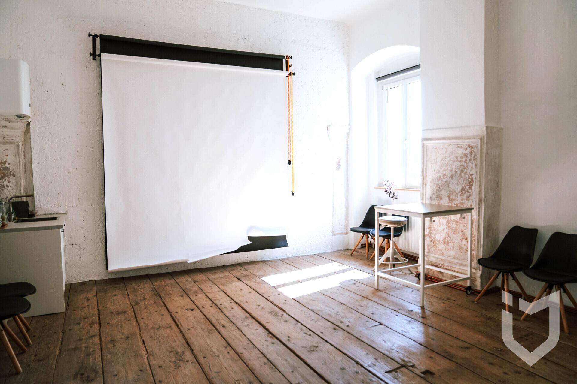 Vielseitiger Raum mit Holzdielenboden, großem Projektionsschirm und einem Fenster, ideal für Präsentationen.