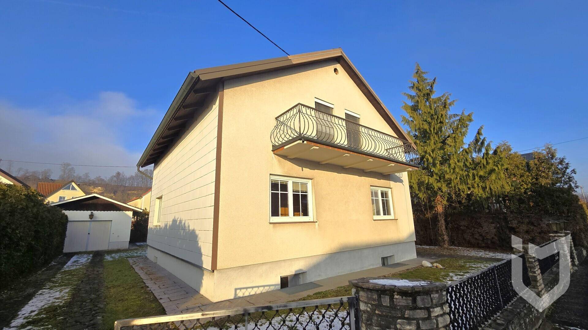 Seitenansicht des Hauses mit Garage und Zufahrt, umgeben von Bäumen und Sträuchern.